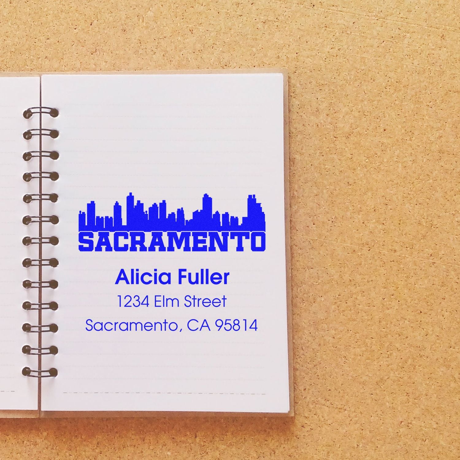 Custom Sacramento return address rubber stamp with skyline design, name, and address on notebook page.