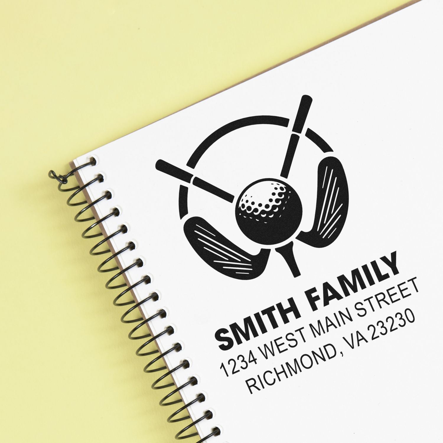 Custom rubber stamp logo for Smith Family golf business with address, shown on a spiral notebook cover.