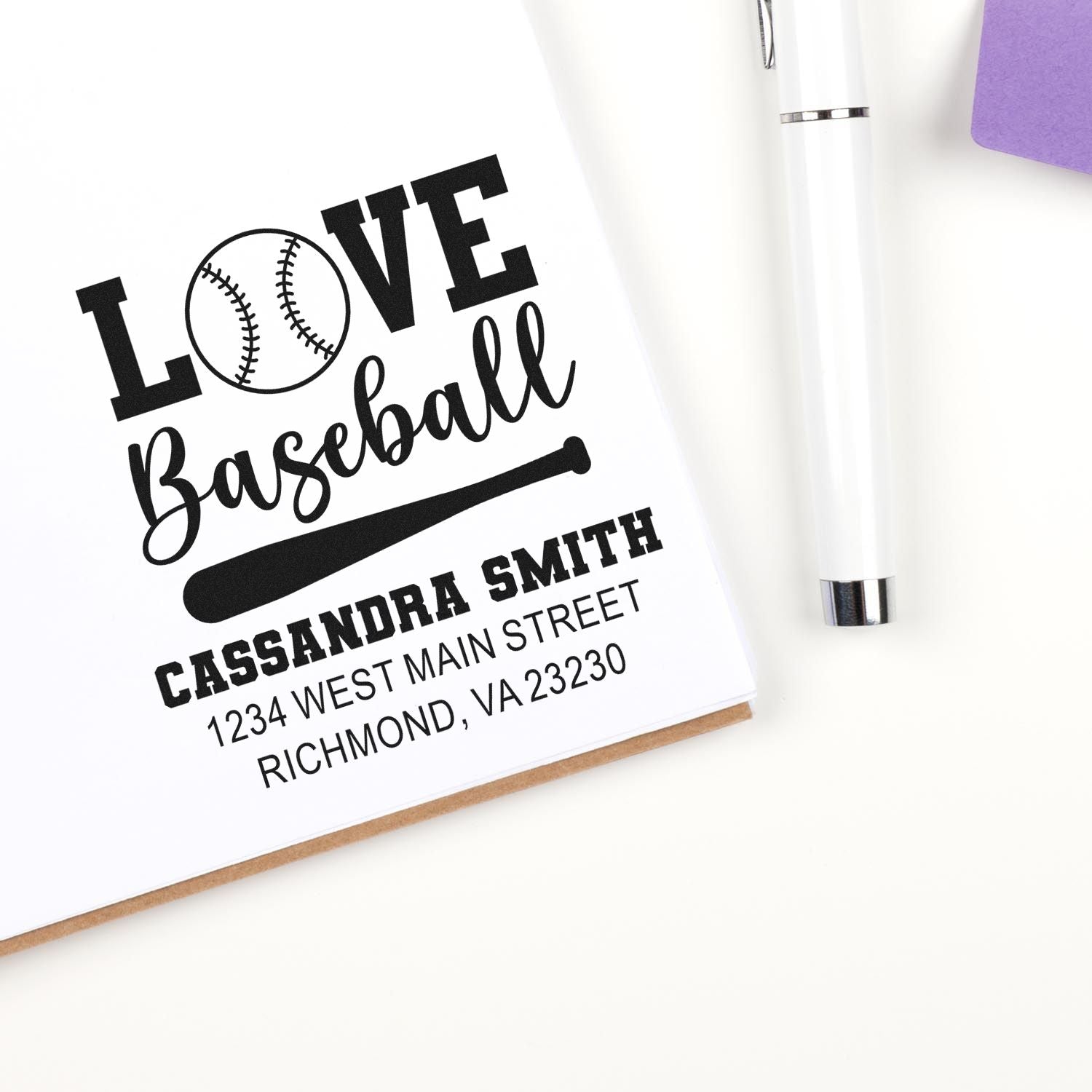 Custom baseball return address rubber stamp with name and address, shown beside a pen on a notebook page.