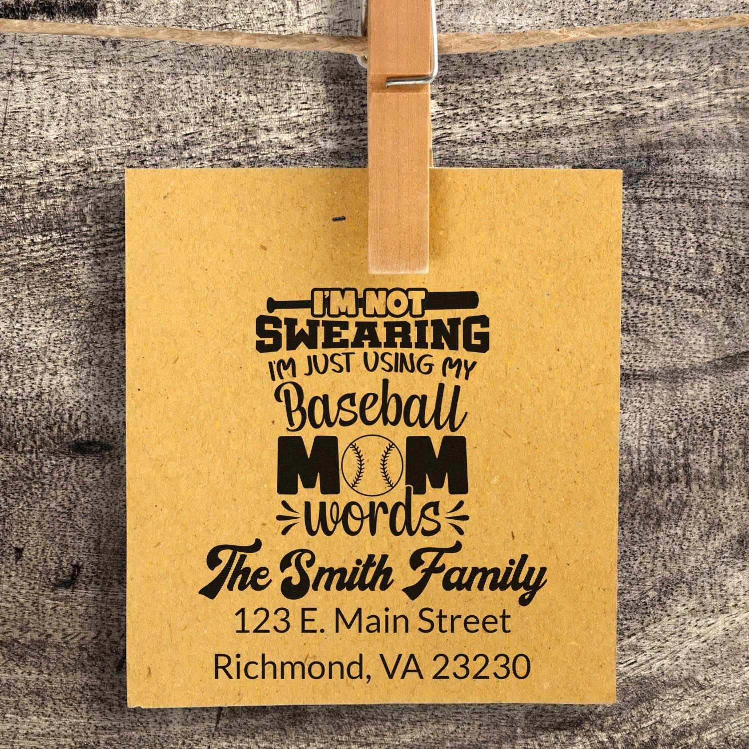 Personalized baseball mom rubber stamp on kraft tag with family name and address, clipped on rustic wood display.