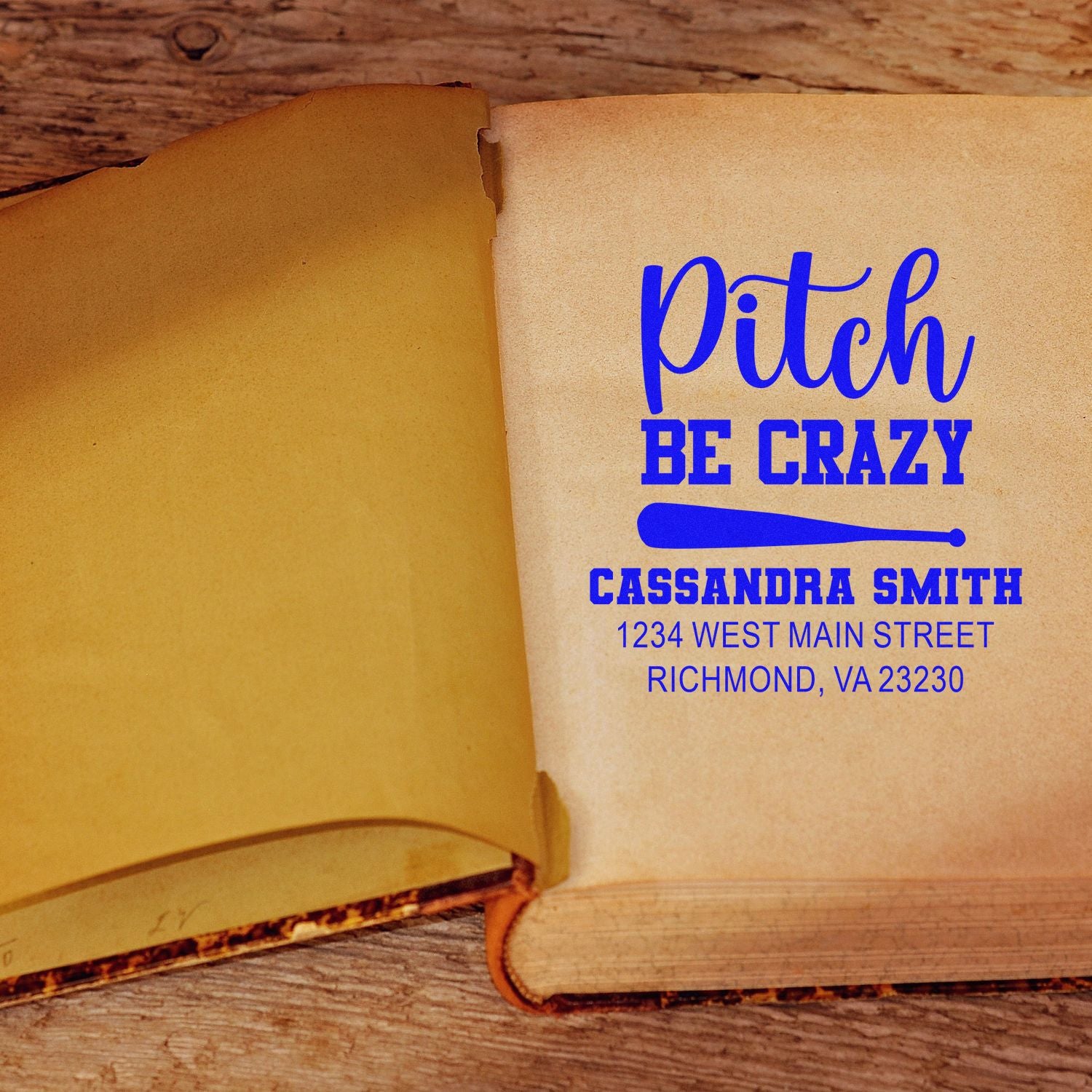 Custom baseball-themed rubber stamp reading Pitch Be Crazy with name and address in blue ink on an open book page.