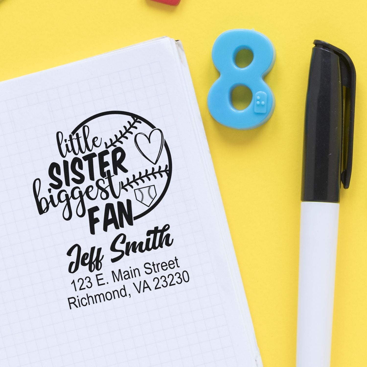 Custom rubber stamp mockup showing a Little Sister Biggest Fan personalized address stamp on a notebook.