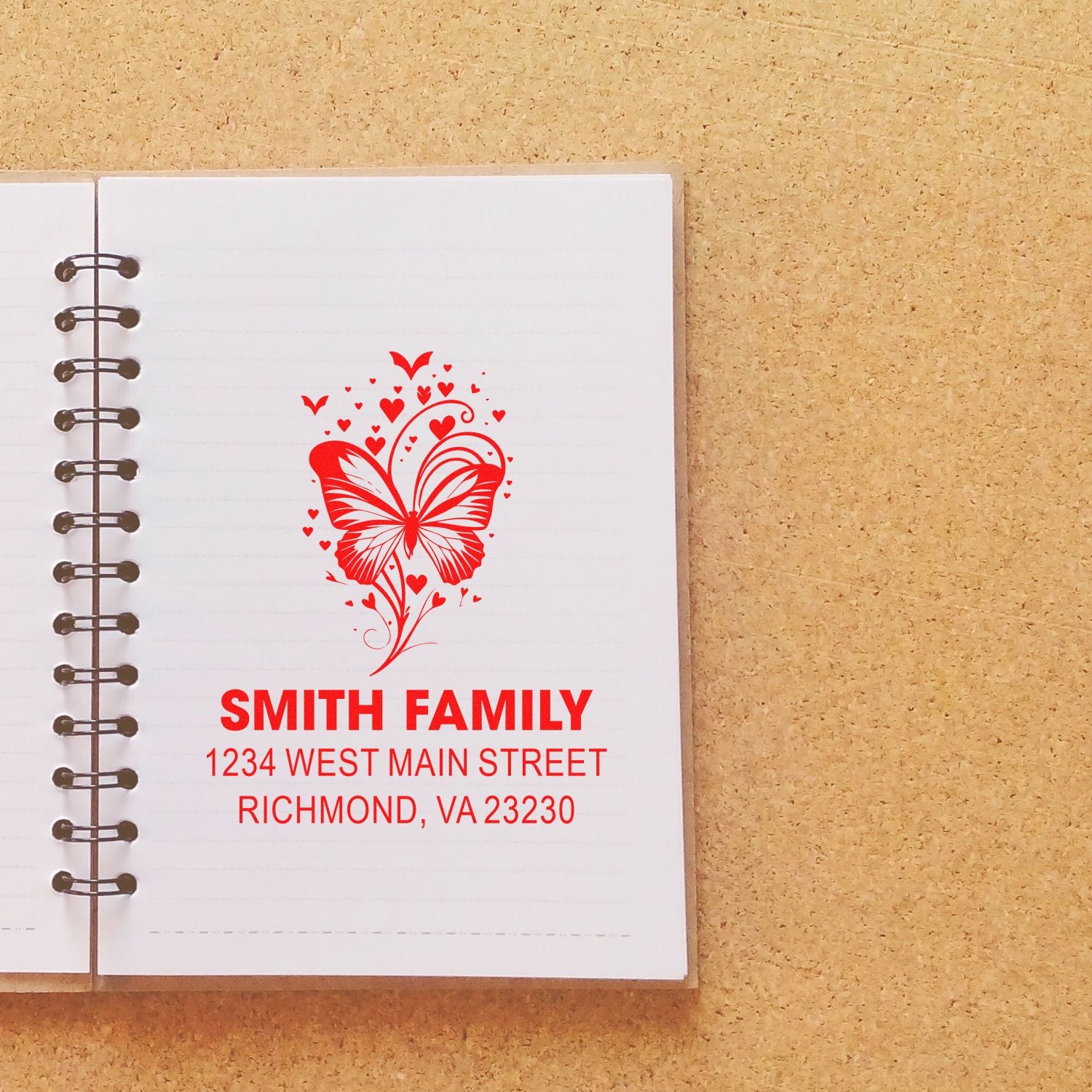 Custom butterfly heart family address rubber stamp in red, showing Smith Family and Richmond, VA on a notebook.