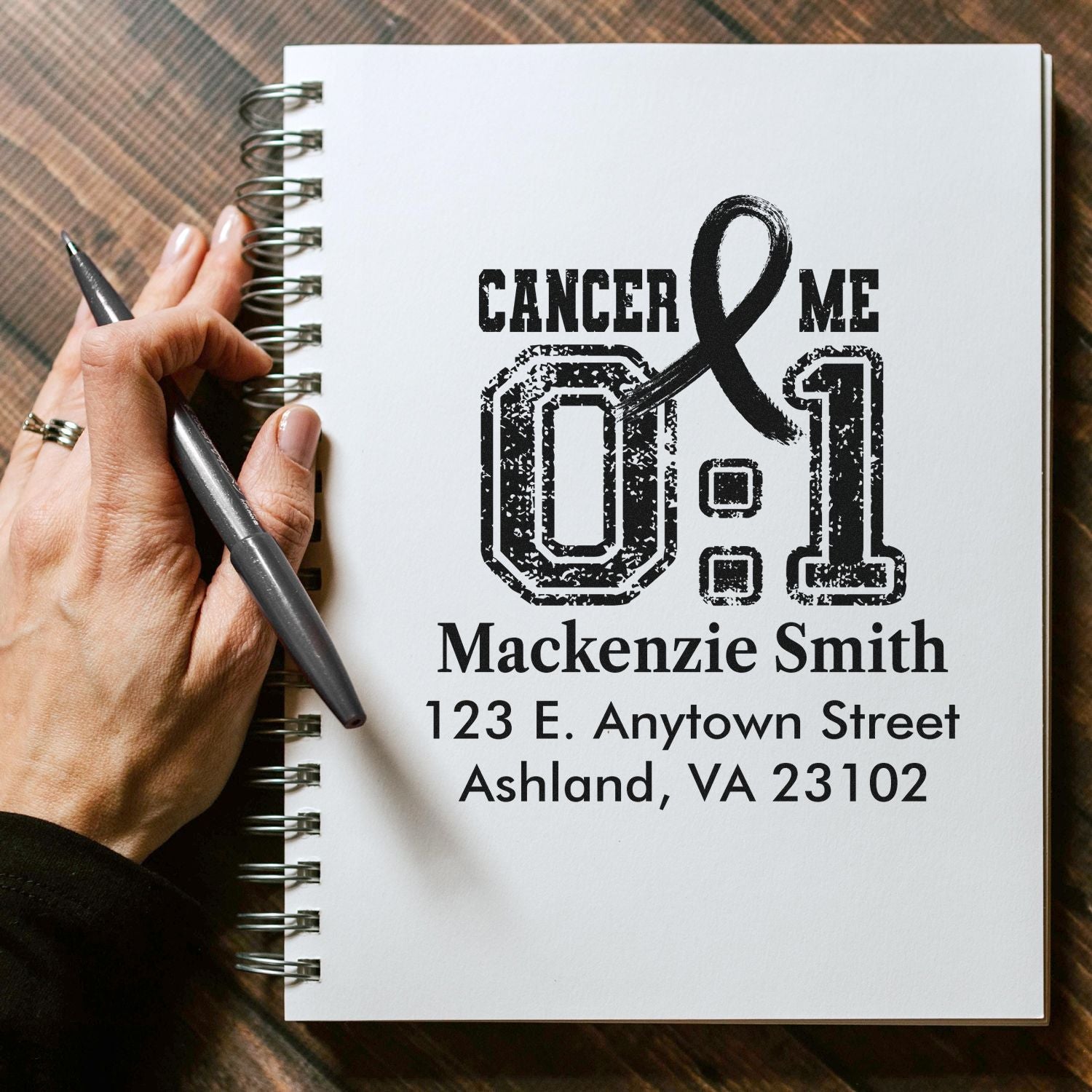 Custom cancer awareness rubber stamp with personalized name and address on notebook mockup.
