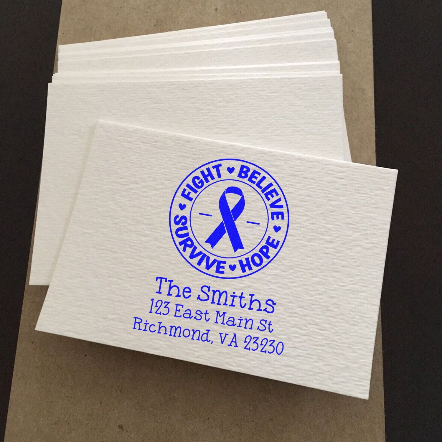 Custom rubber stamp on white napkins with Fight Believe Survive Hope ribbon design and personalized family address.