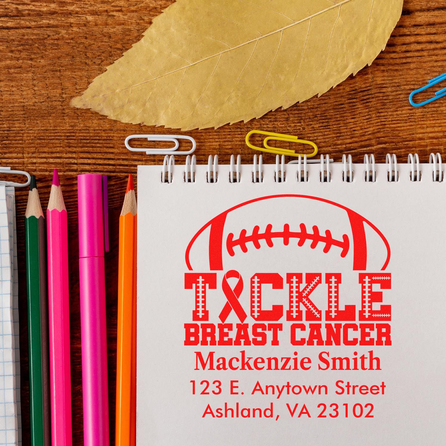 Personalized breast cancer awareness rubber stamp with football motif, name, and address on a notebook.