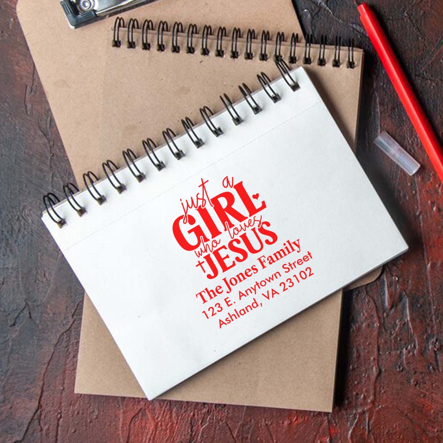 Custom rubber stamp design on spiral notebook featuring Just a Girl Who Loves Jesus with personalized family address details.