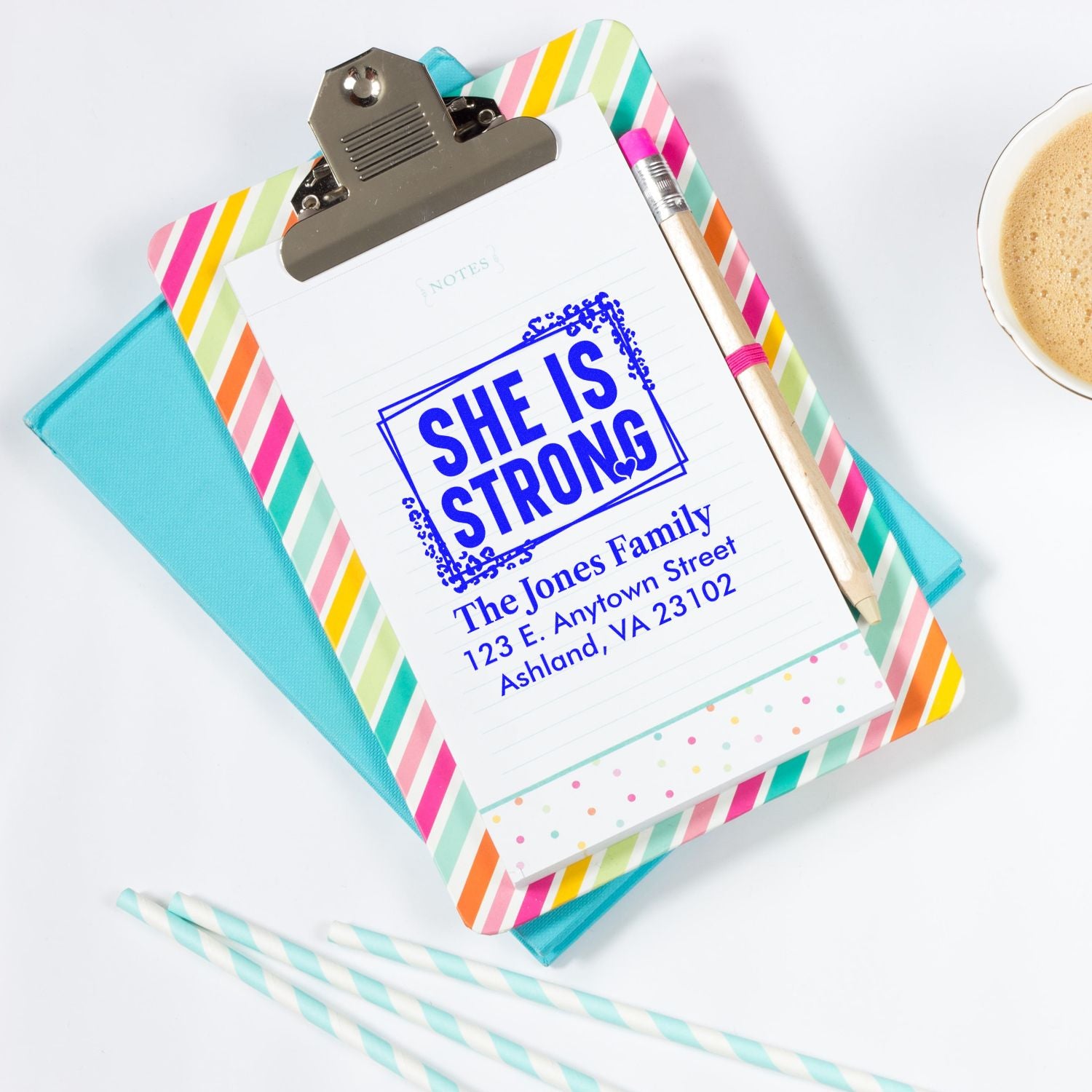 Personalized rubber stamp reading She Is Strong with family name and address on a clipboard for custom stationery.