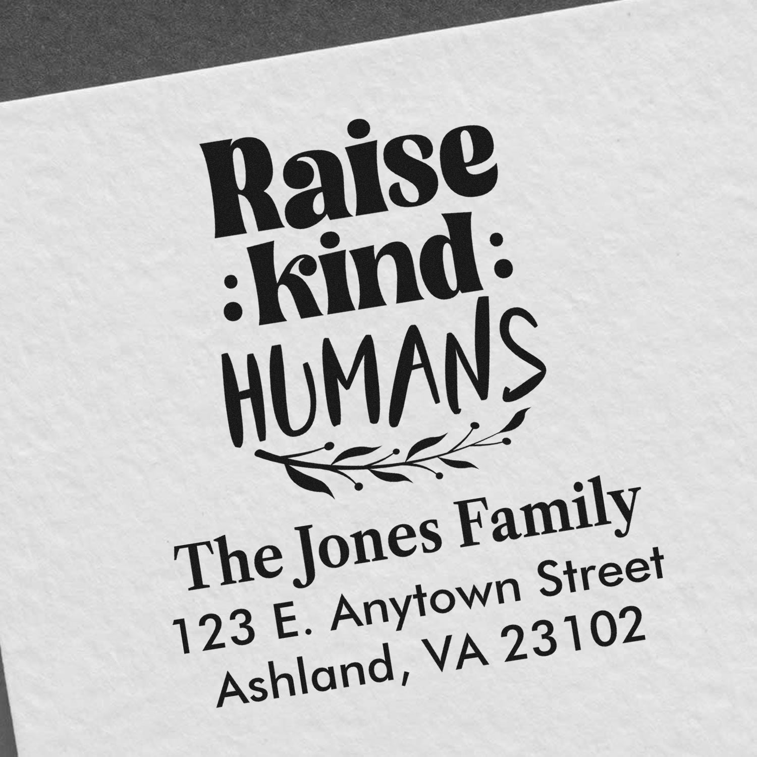 Custom rubber stamp reading Raise kind humans with personalized family name and return address for mailings and gifts.