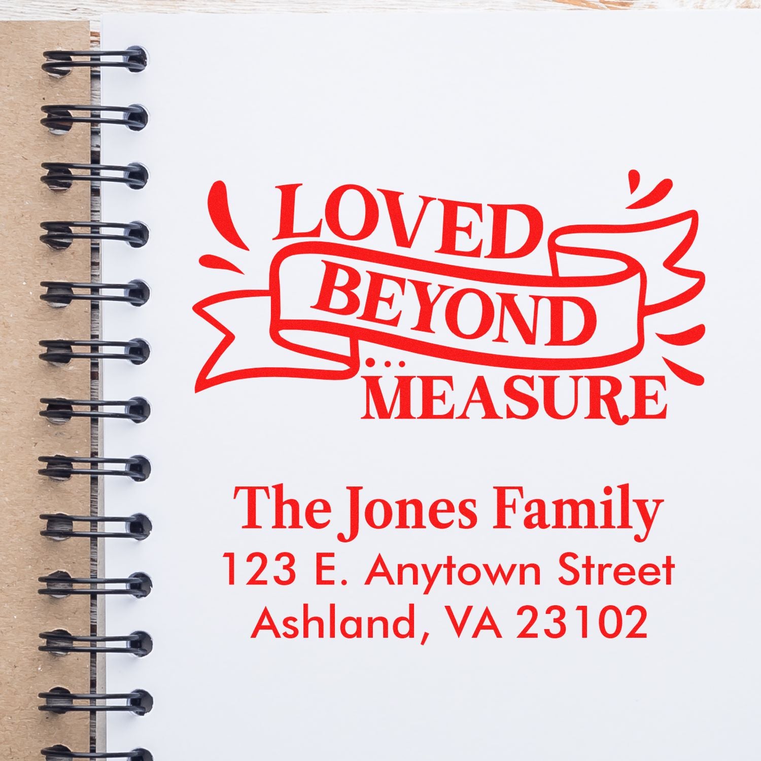 Custom rubber stamp mockup with Loved Beyond Measure and The Jones Family address on a spiral notebook page.