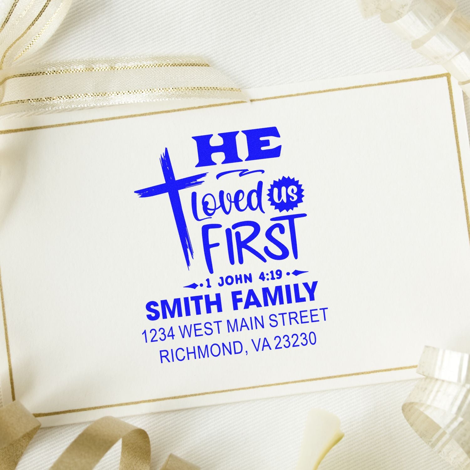 Personalized Christian return address rubber stamp with cross, He Loved Us First verse, and family name for wedding stationery.