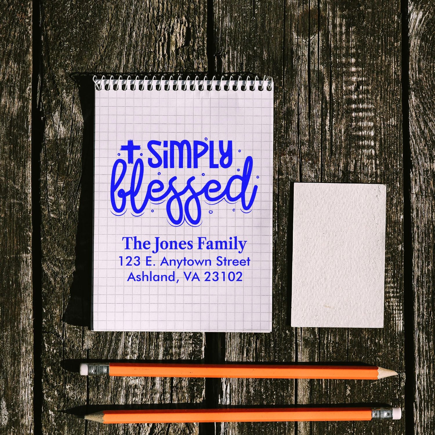 Custom religious return address rubber stamp mockup with Simply Blessed for The Jones Family, blue imprint on notebook.