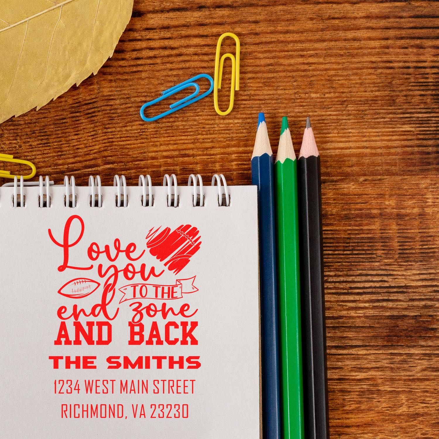 Custom football-themed rubber stamp on notepad with Love you to the end zone and back, family name, and address.