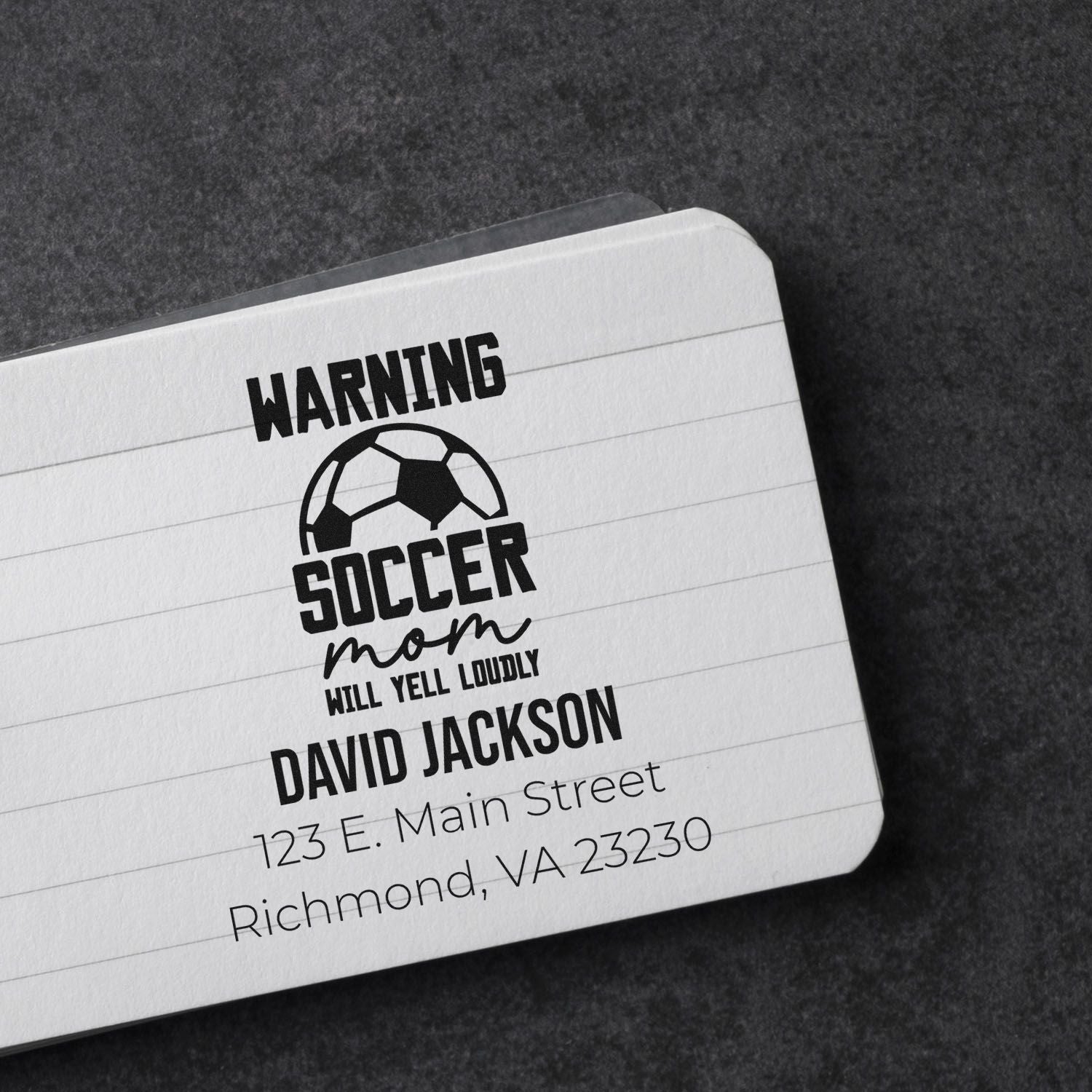 Custom soccer mom rubber stamp with warning design, personalized name and address, shown on a notebook.