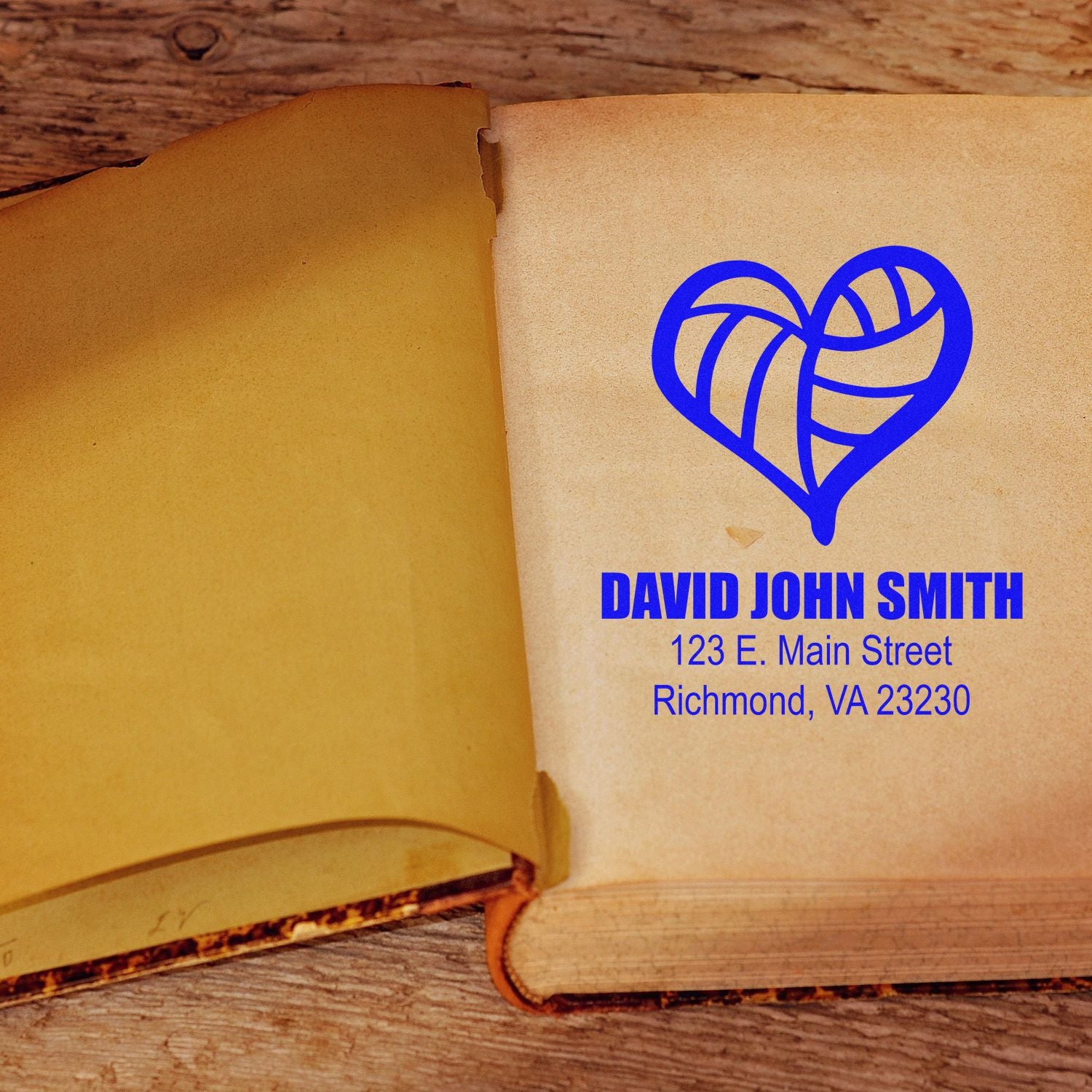 Custom bookplate rubber stamp with blue heart logo, name, and address on an open book page.