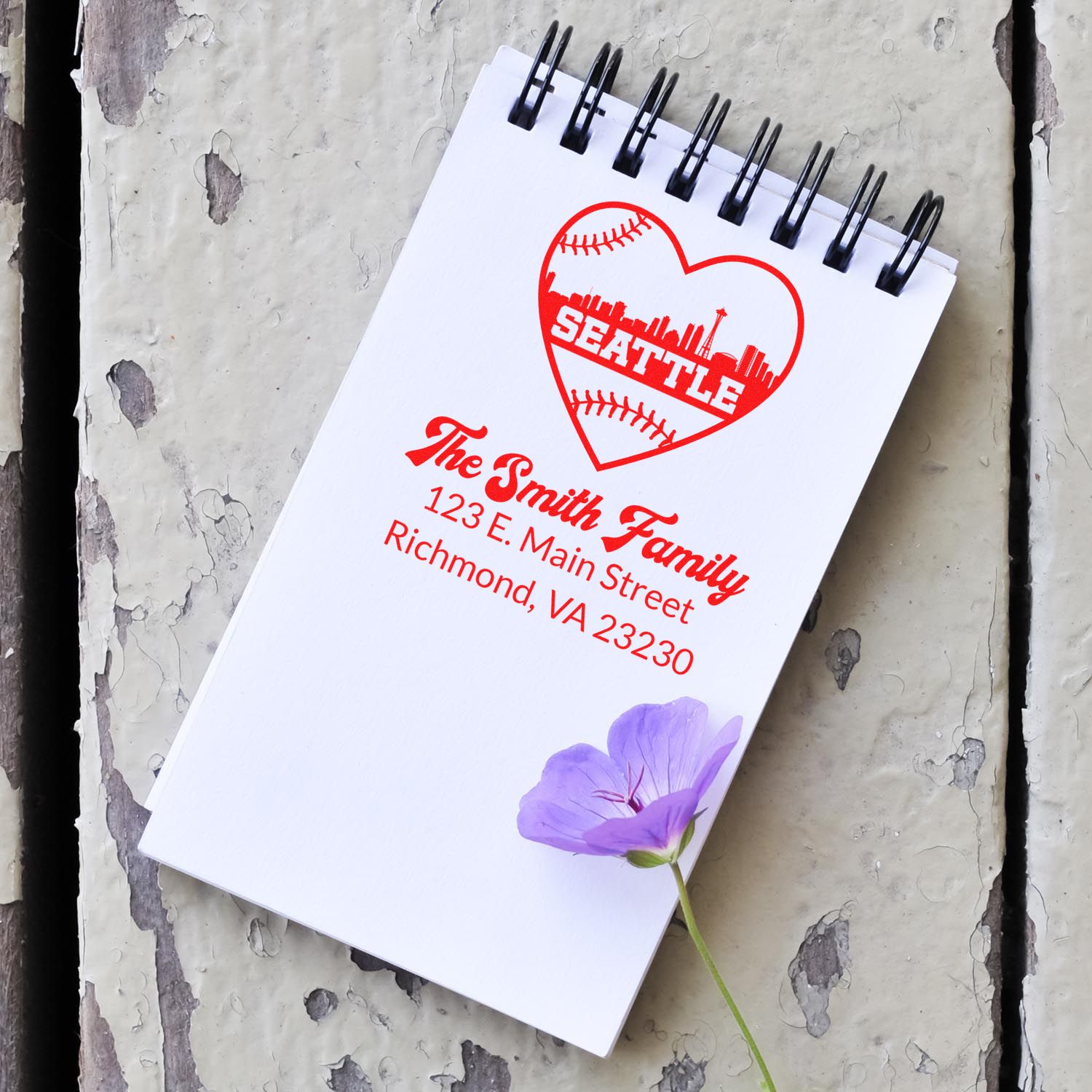 Custom address rubber stamp mockup with Seattle heart baseball design and family name imprint on a notebook.
