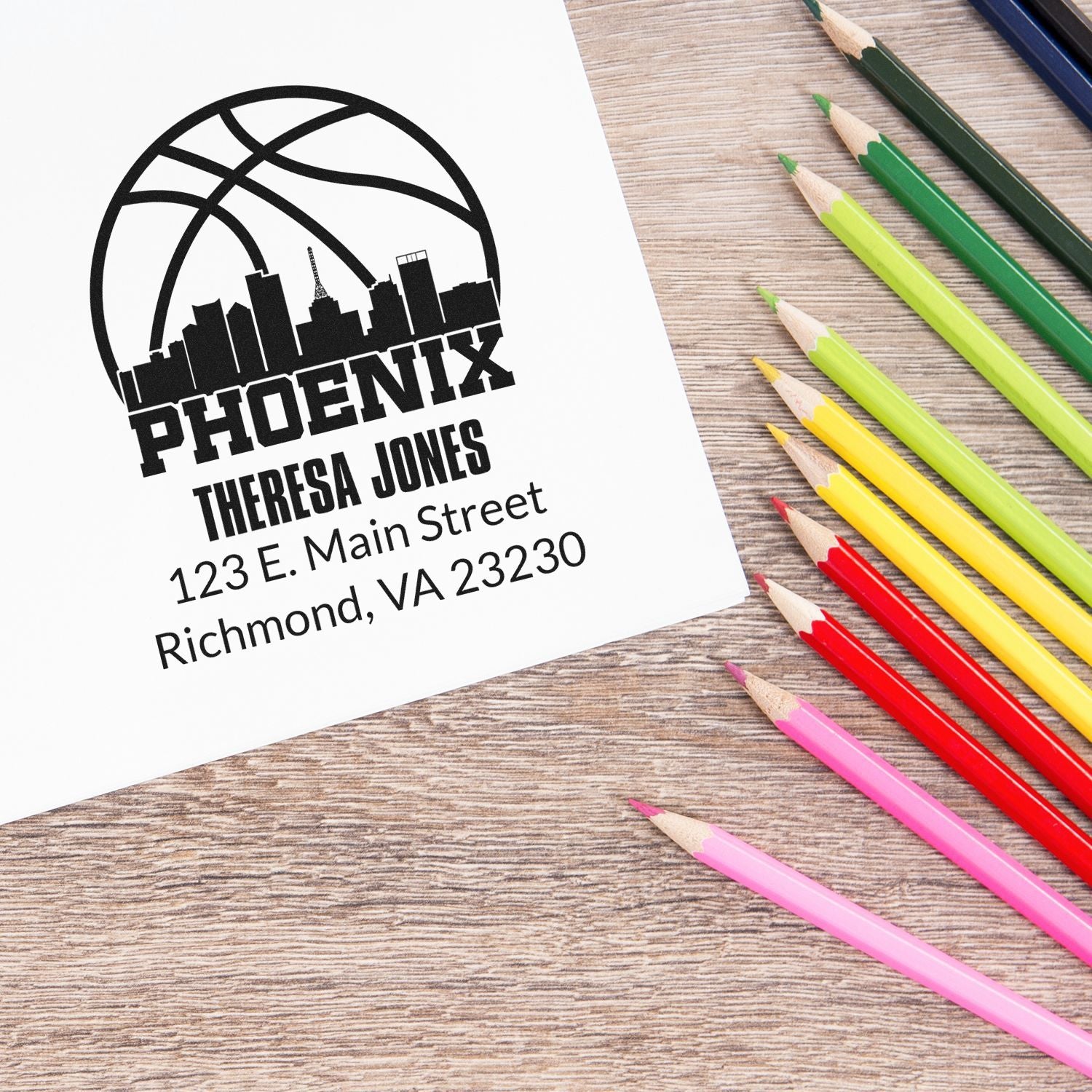 Custom Phoenix rubber stamp design with name and address, shown beside colorful pencils on a wooden desk