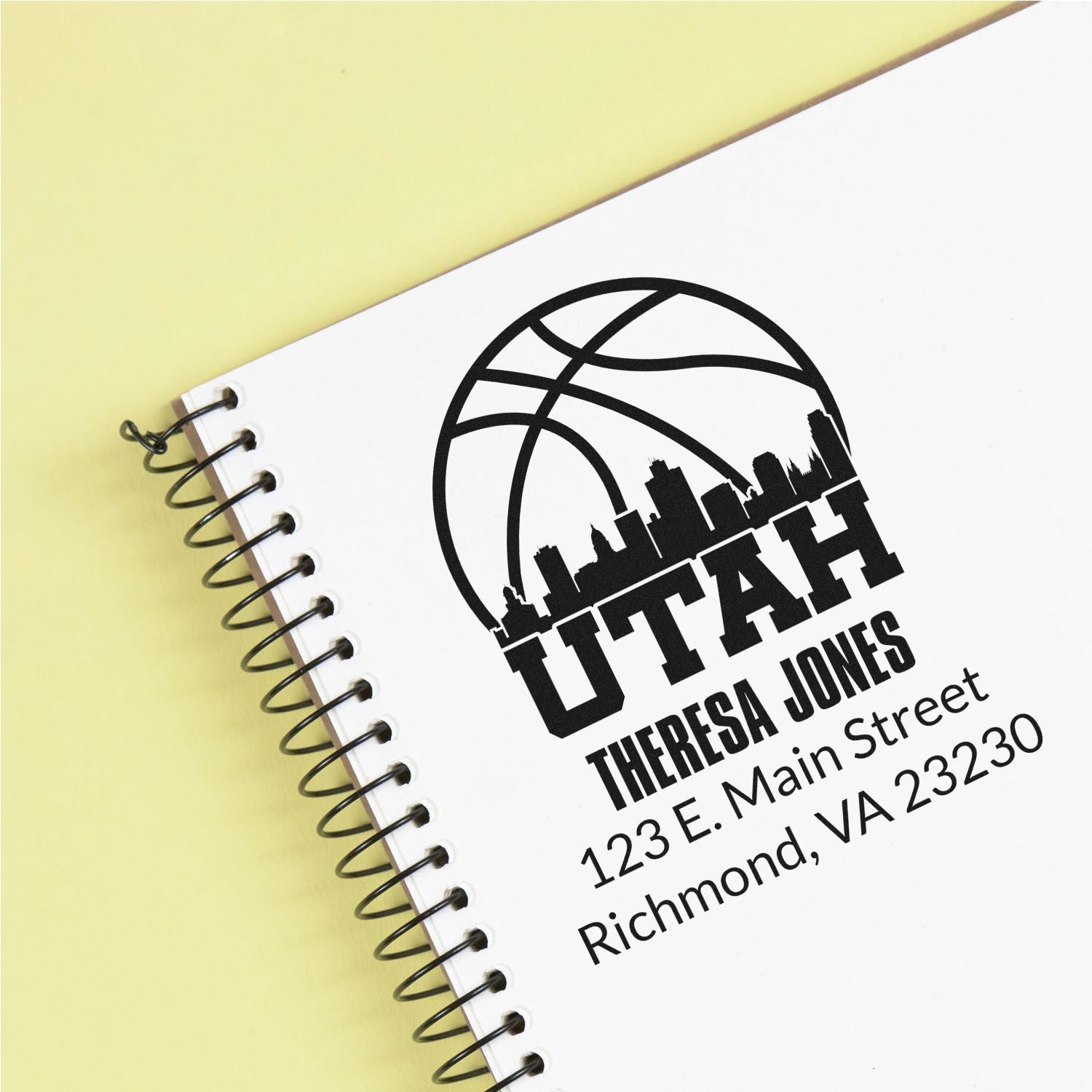 Custom rubber address stamp for Theresa Jones with Utah basketball logo, imprinted on a spiral notebook.