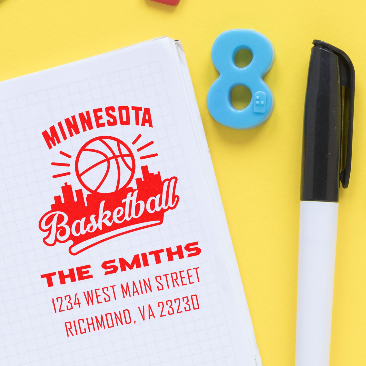 Custom basketball rubber stamp design printed on notebook, with Minnesota text and address, beside a marker on yellow background.