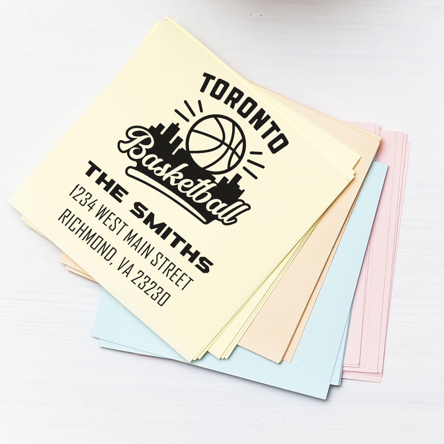 Custom rubber stamp with basketball logo and Toronto address, stamped on pastel paper sheets.