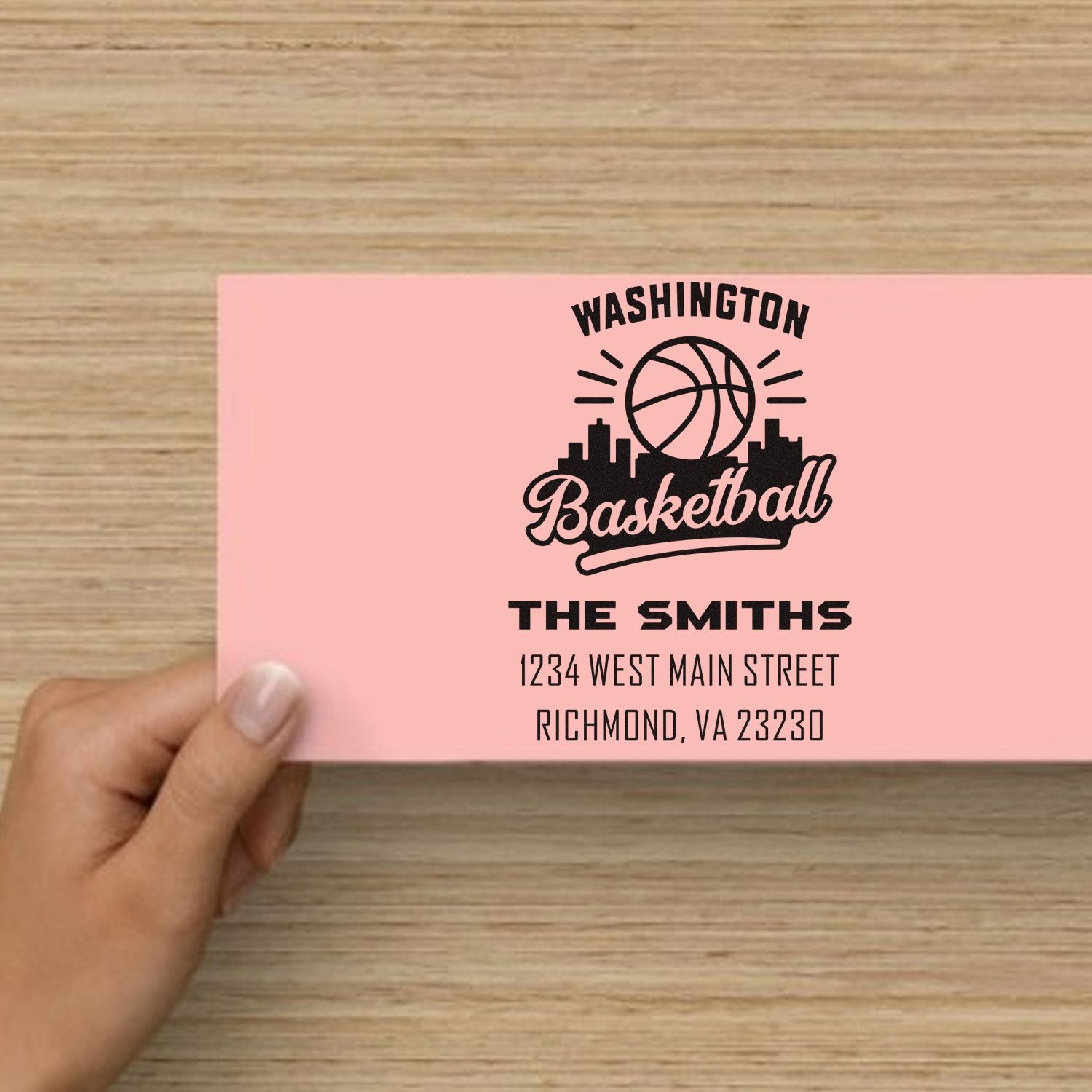 Personalized rubber stamp for Washington Basketball mailers, featuring The Smiths family name and address on a pink envelope.