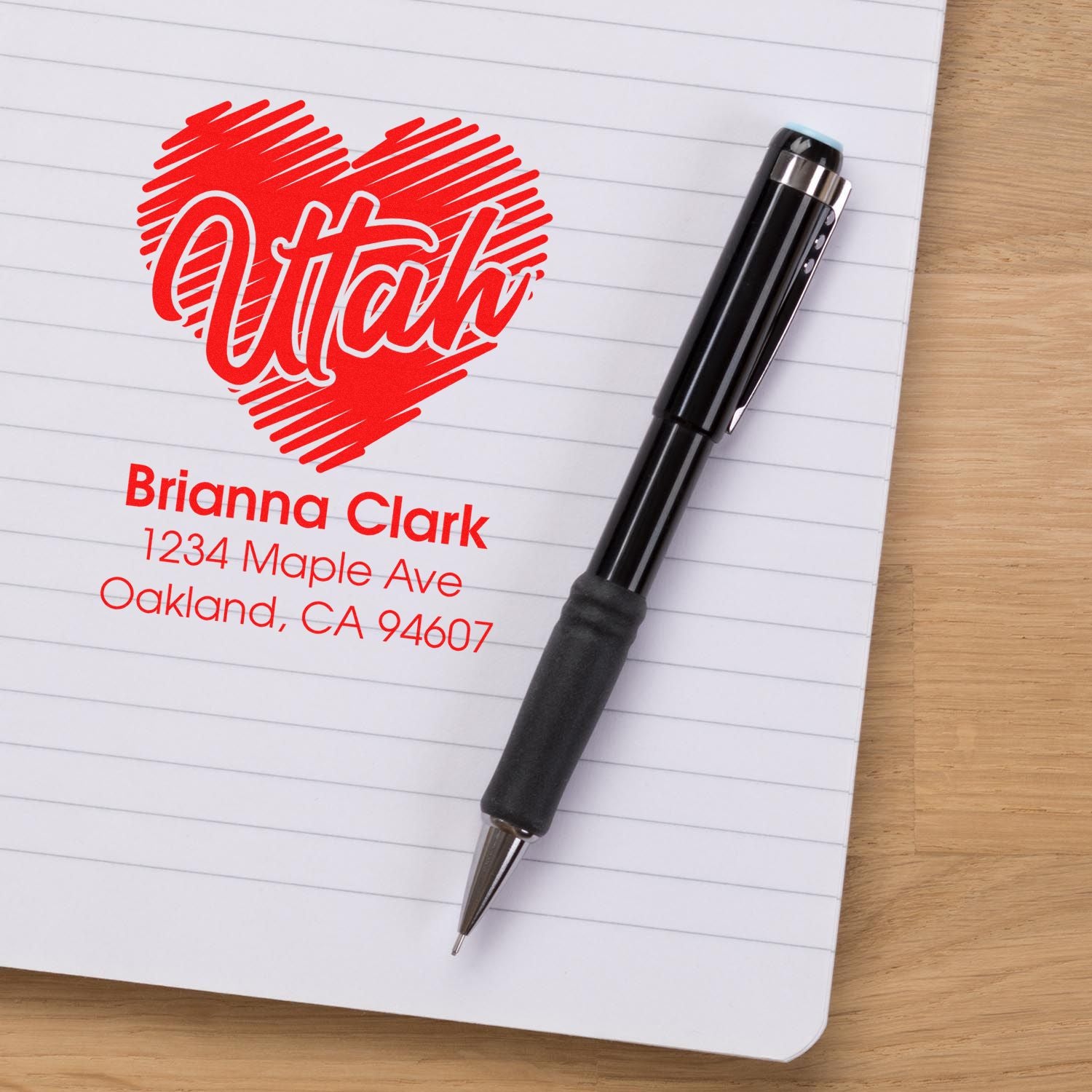Custom return address rubber stamp with Utah heart design on a notebook beside a pen