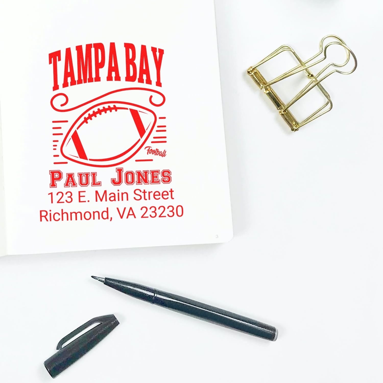 Custom Tampa Bay football rubber stamp with Paul Jones name and Richmond, VA address, shown with pen and binder clip.