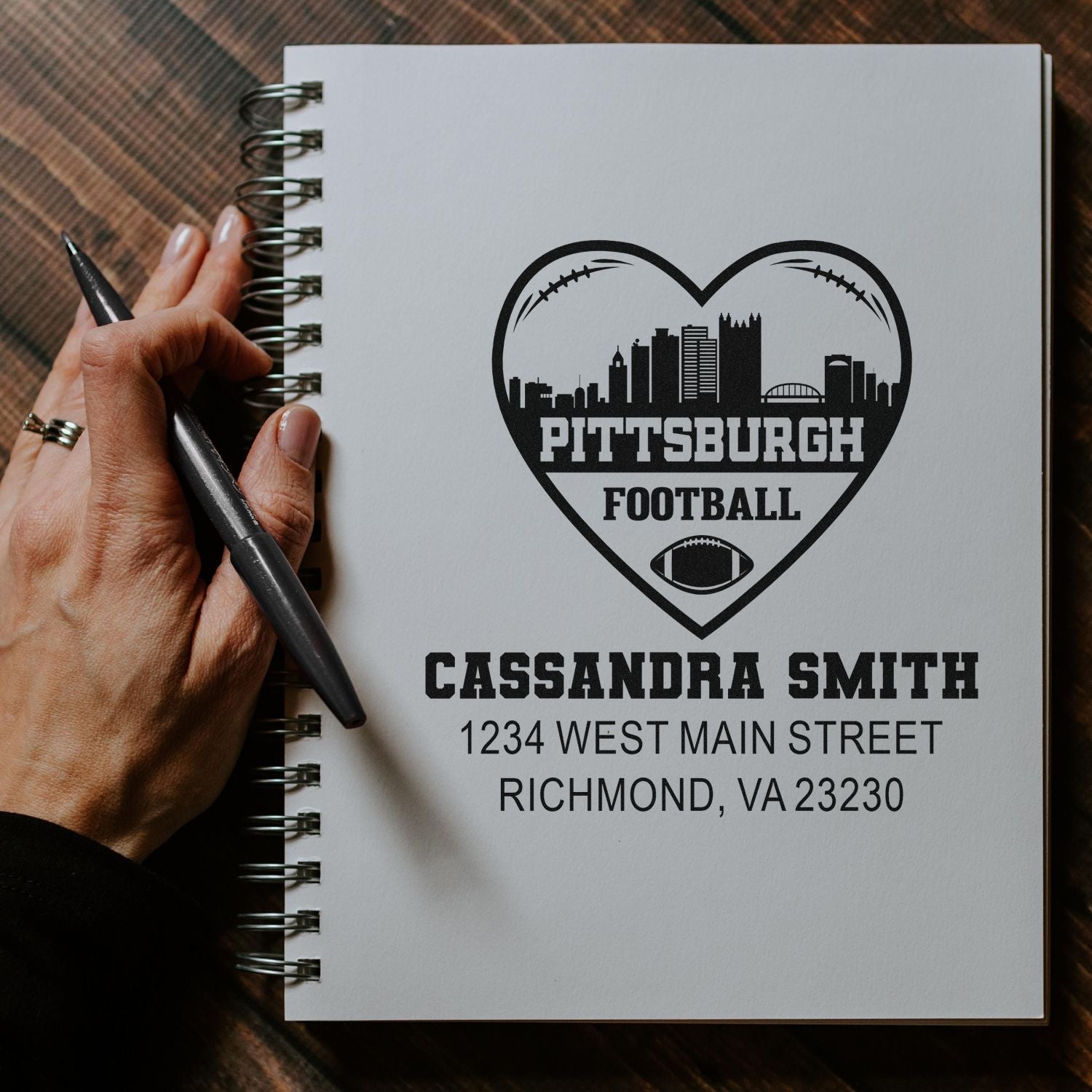 Custom rubber stamp design on a notebook with Pittsburgh football heart logo, personalized with Cassandra Smith and address.
