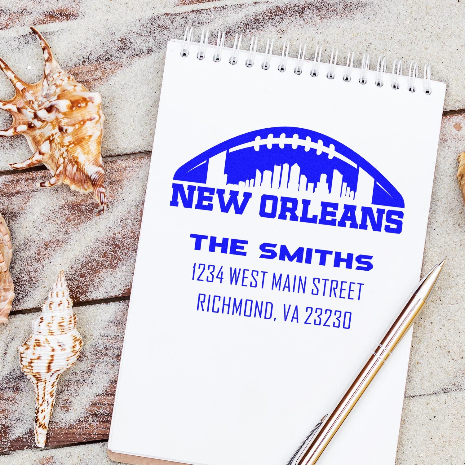 Custom rubber address stamp with New Orleans skyline football logo, family name, and address on a notebook.