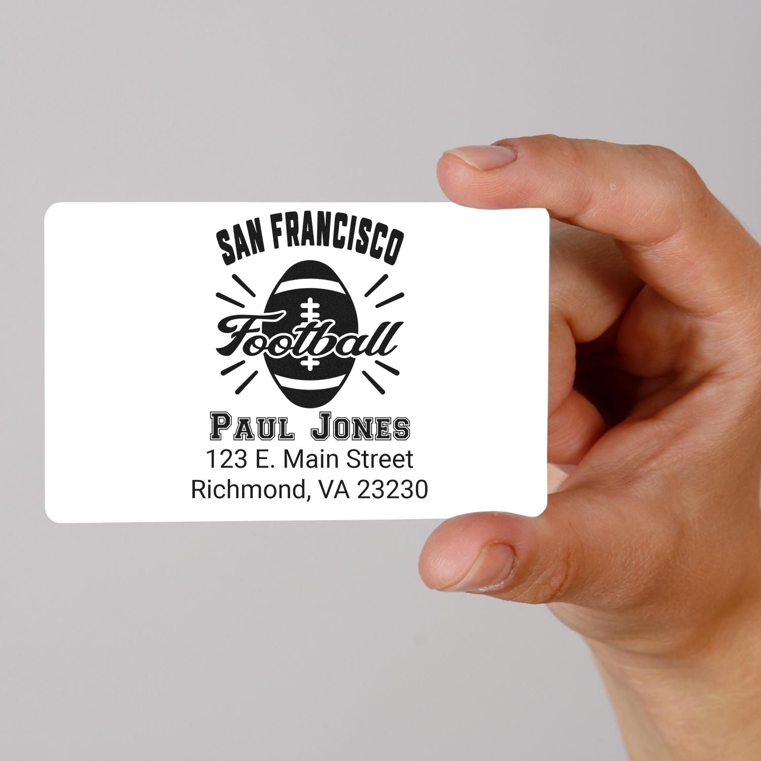 Hand holding custom football address stamp design with San Francisco Football logo, Paul Jones name, and mailing address.