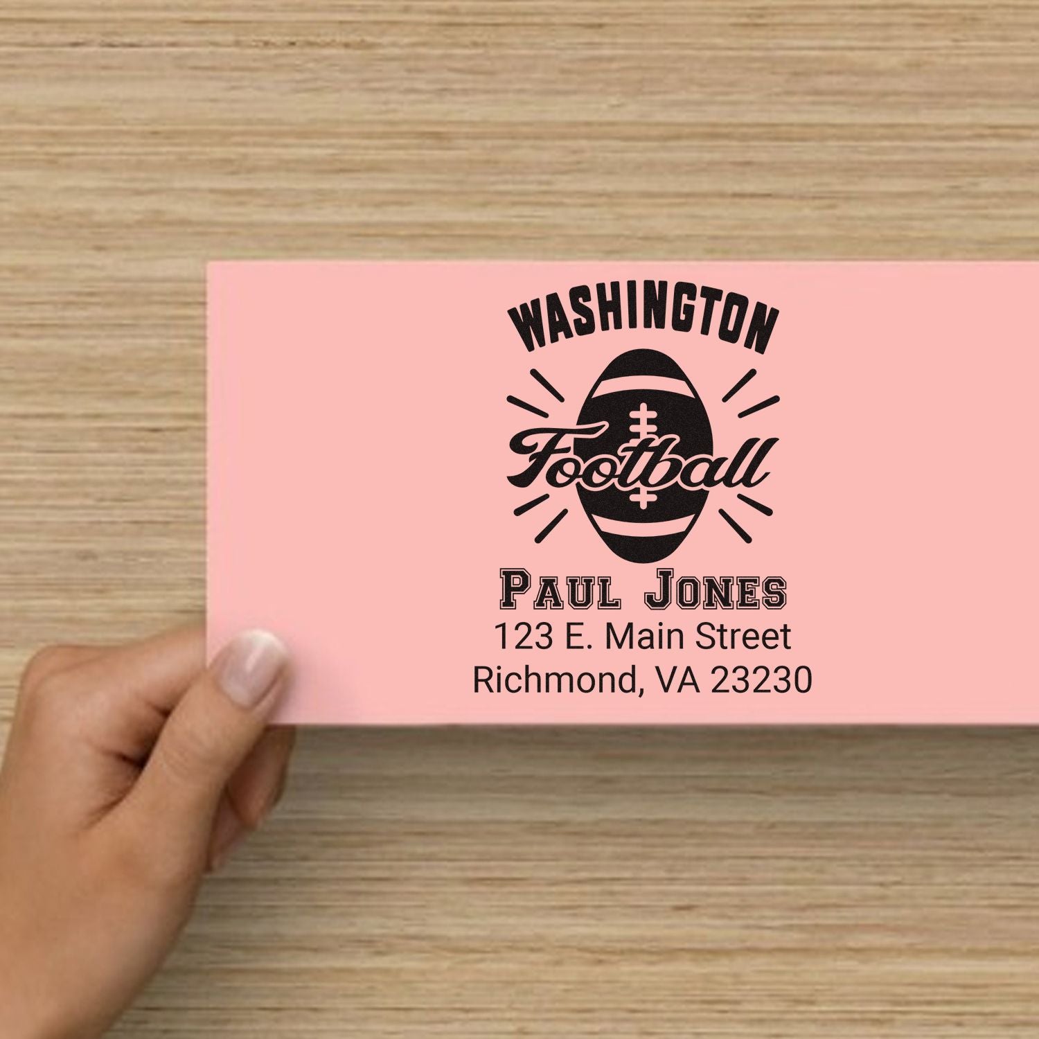 Personalized Washington football rubber stamp with name and address on pink card, held in hand.