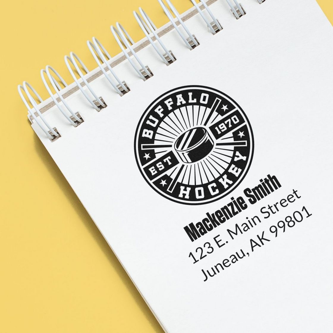 Custom rubber stamp with hockey logo, name, and address imprint on notebook for personalized business branding.