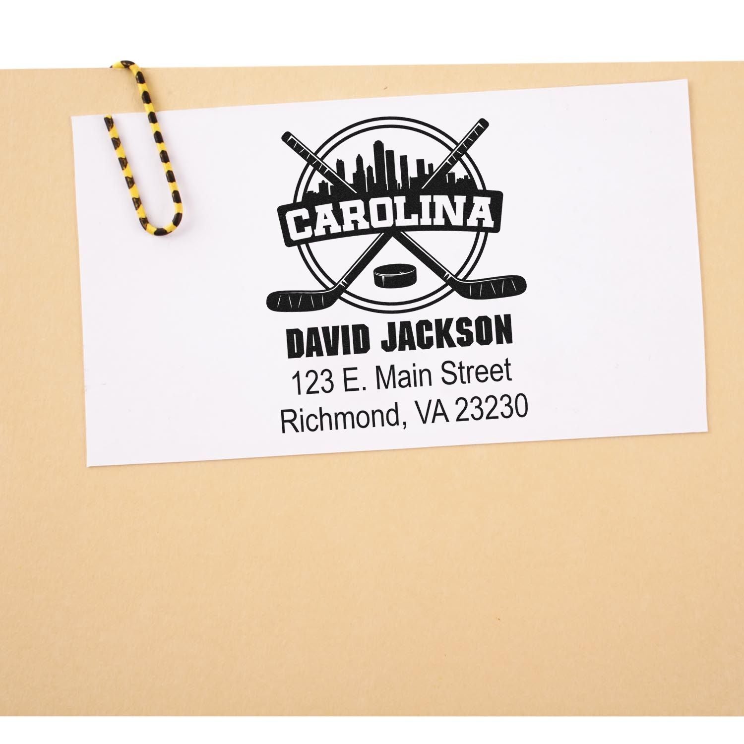Custom hockey rubber stamp design with Carolina logo, name, and address on paper clipped to a file folder.
