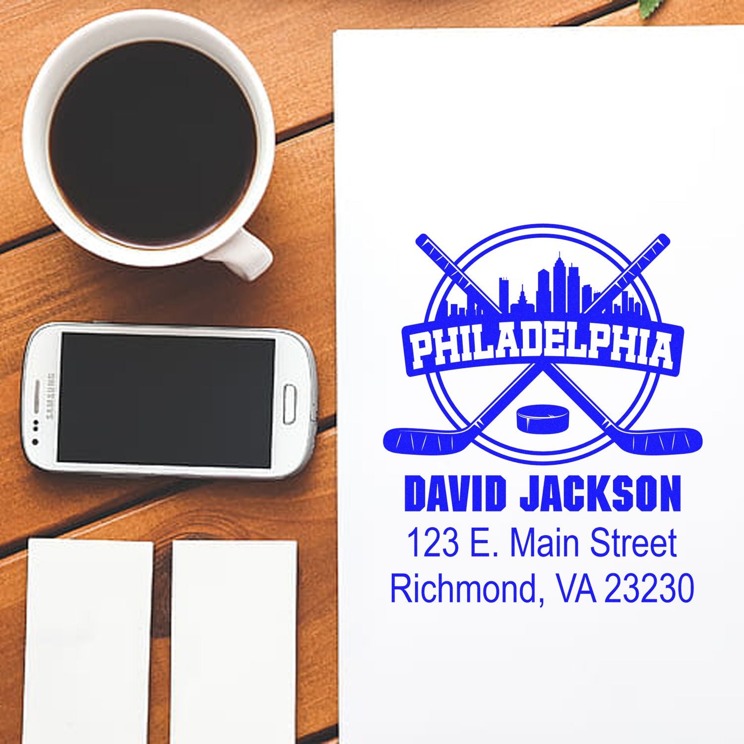 Custom Philadelphia hockey return address rubber stamp with name, address, and logo on paper, shown with coffee, phone, and cards.