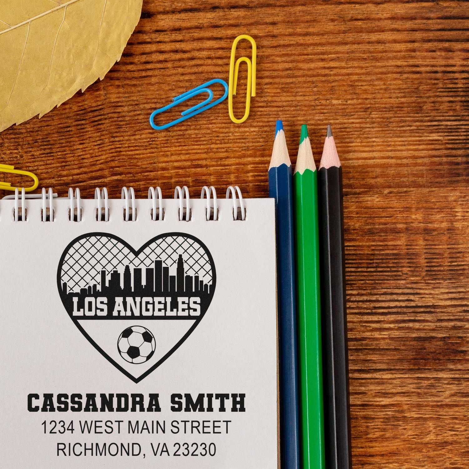 Custom rubber stamp mockup on notebook featuring Los Angeles soccer heart, personalized address stamp for Cassandra Smith.