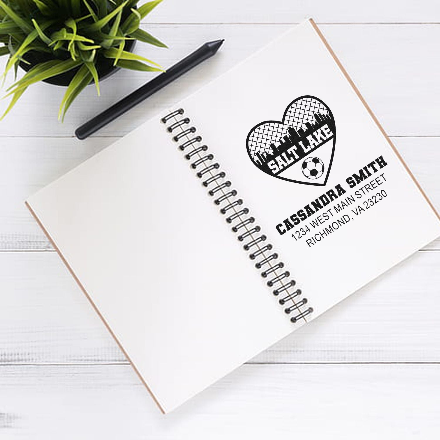 Custom rubber stamp mockup with Salt Lake heart logo and personalized address stamp on a notebook.