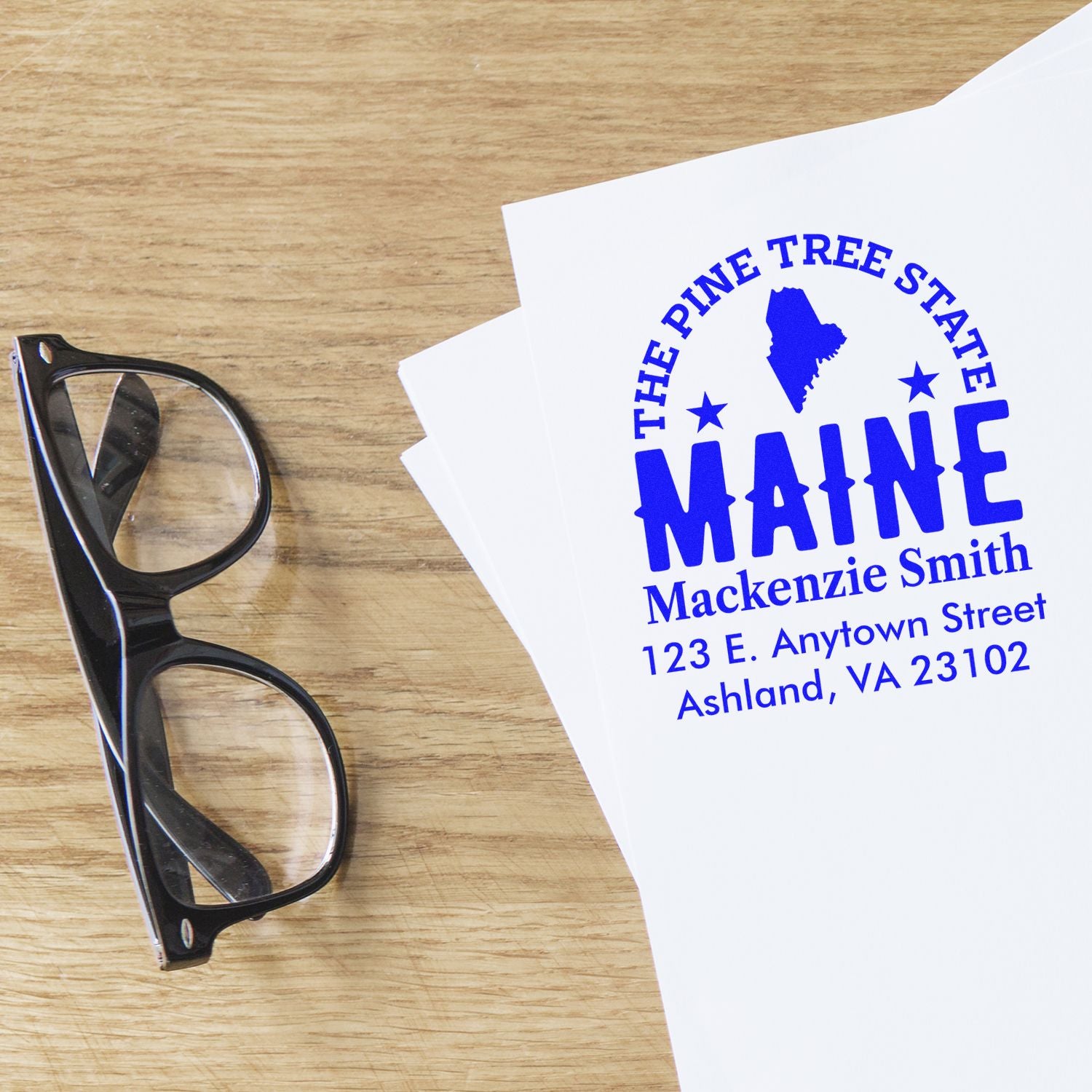 Personalized Maine return address rubber stamp with Pine Tree State design on stationery and blue ink imprint.