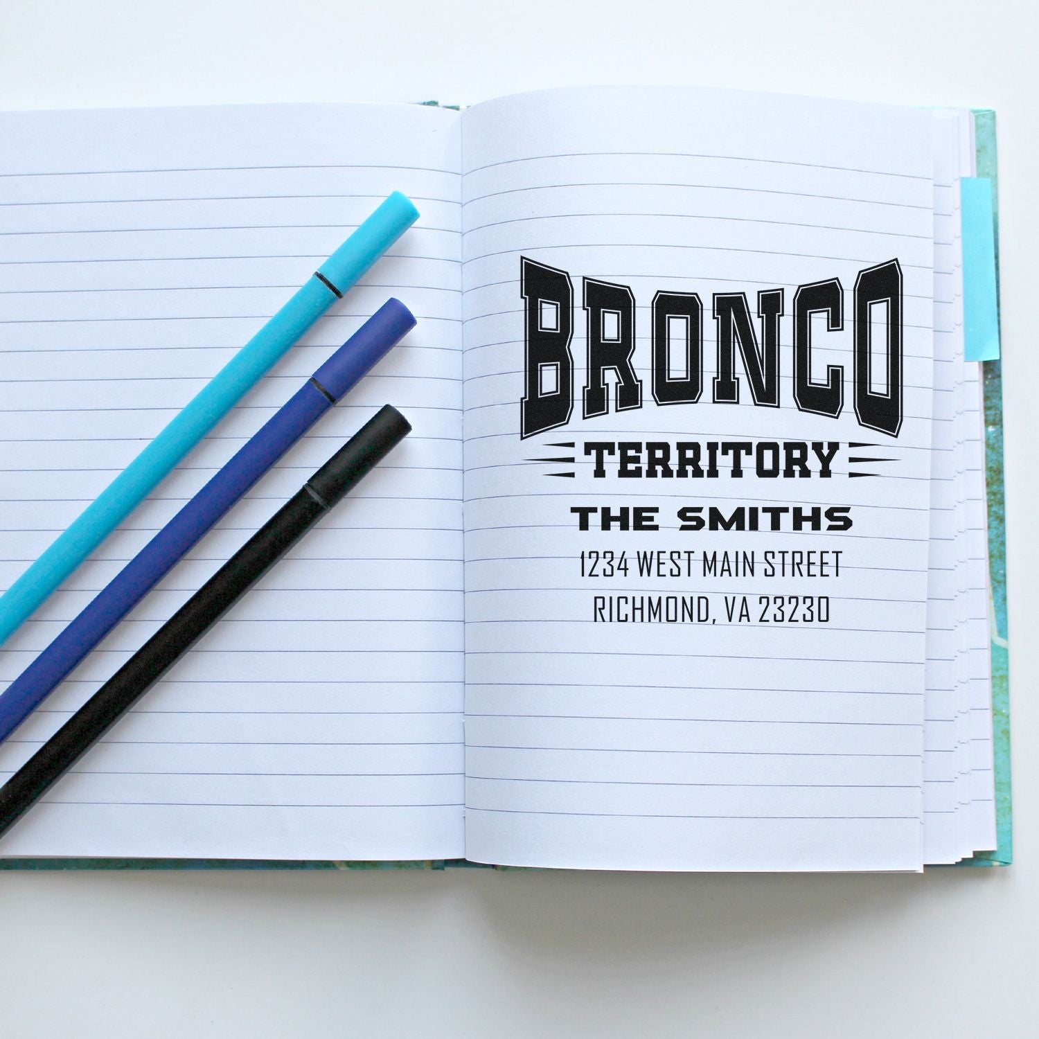 Custom address rubber stamp impression reading Bronco Territory, The Smiths, with name and address in a notebook.