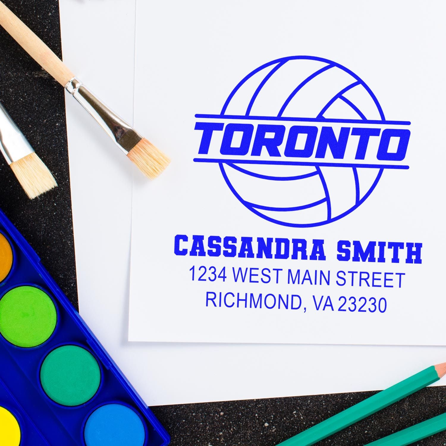 Custom rubber stamp with Toronto logo, name, and address on paper, shown with art supplies for branding and packaging.
