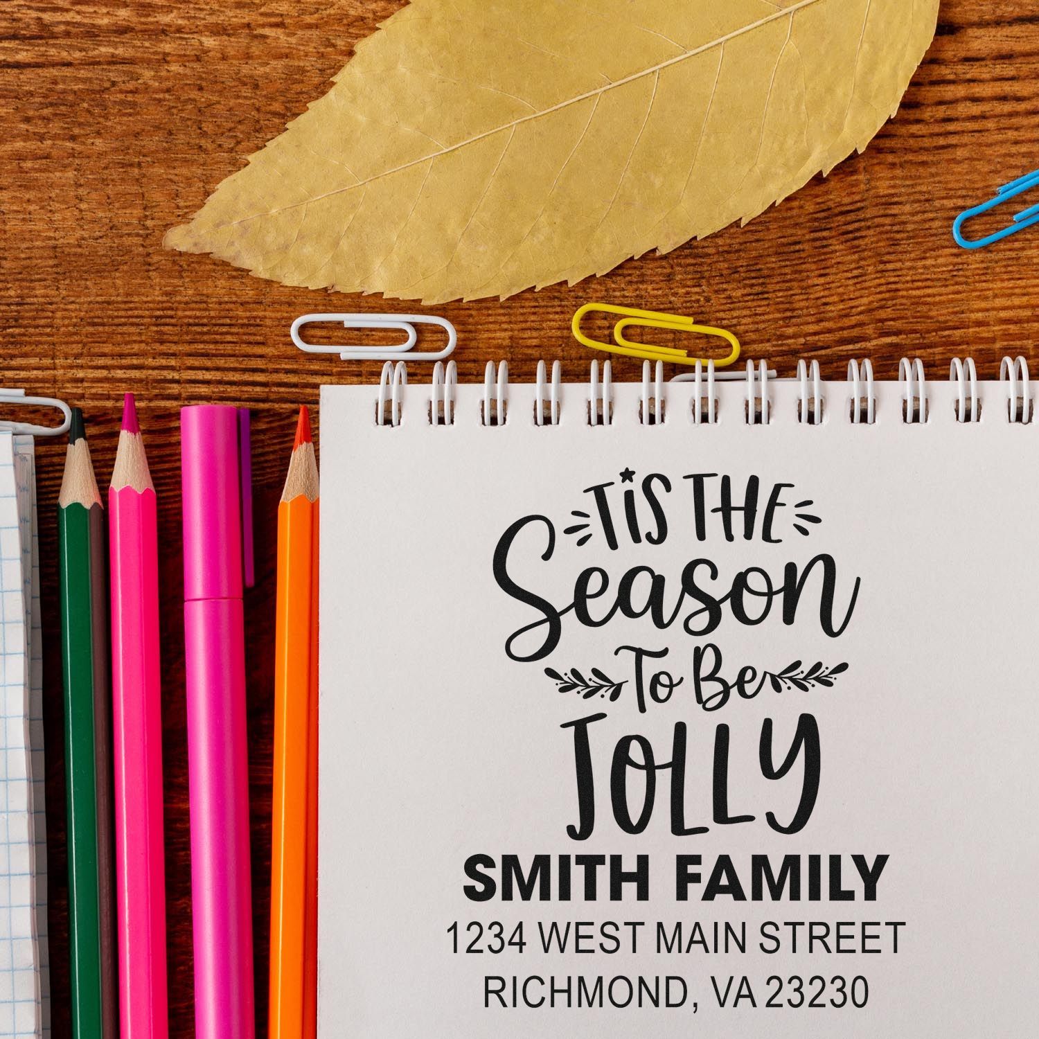 Custom rubber stamp for holiday stationery with Tis the Season to Be Jolly family address design on a notebook.