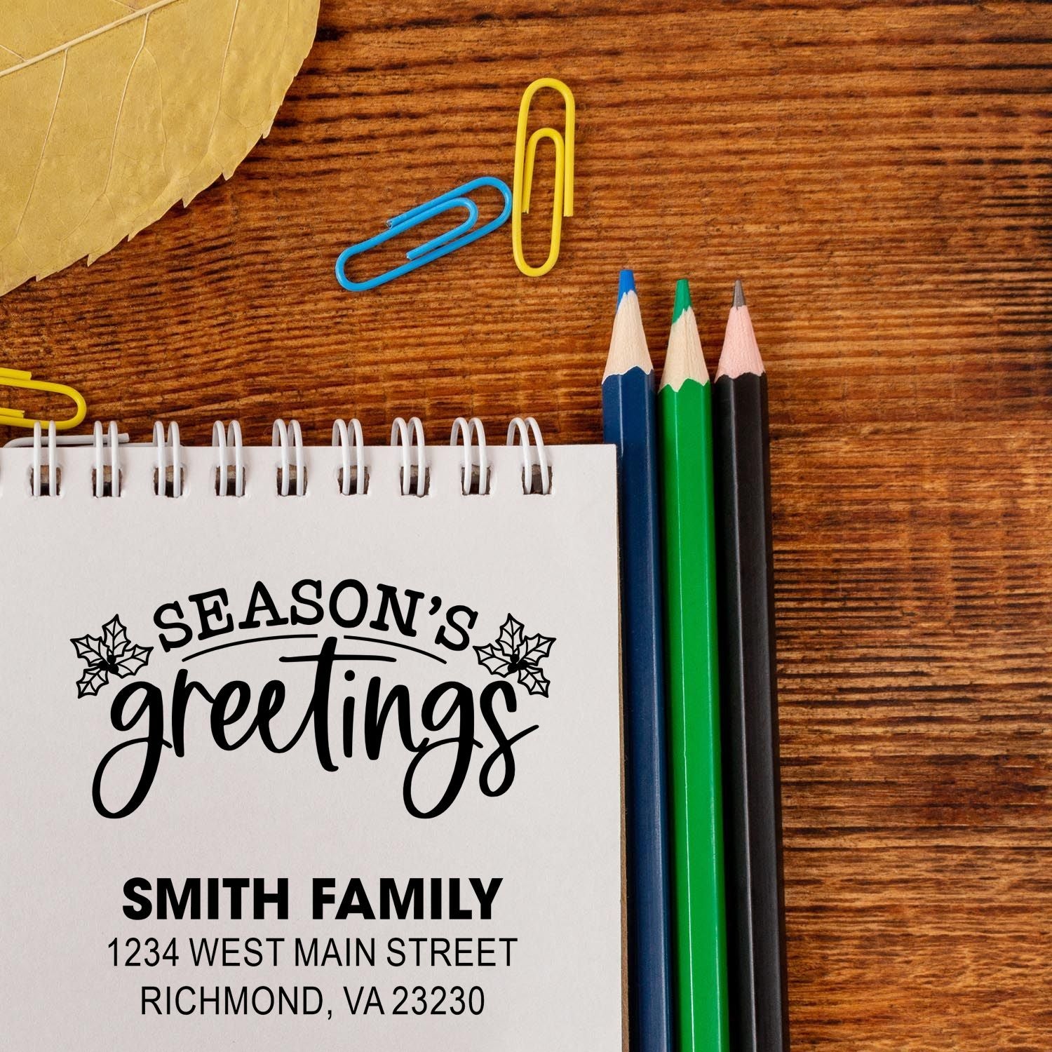 Custom holiday address rubber stamp mockup with Seasons Greetings and Smith family address on notebook paper.