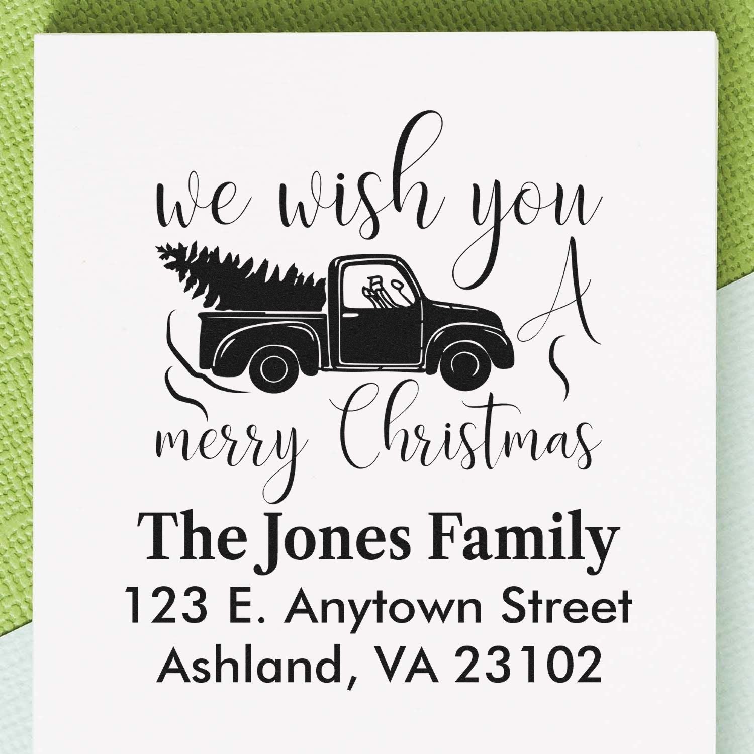 Personalized Christmas rubber stamp with truck and tree, We Wish You a Merry Christmas, family name, and return address.
