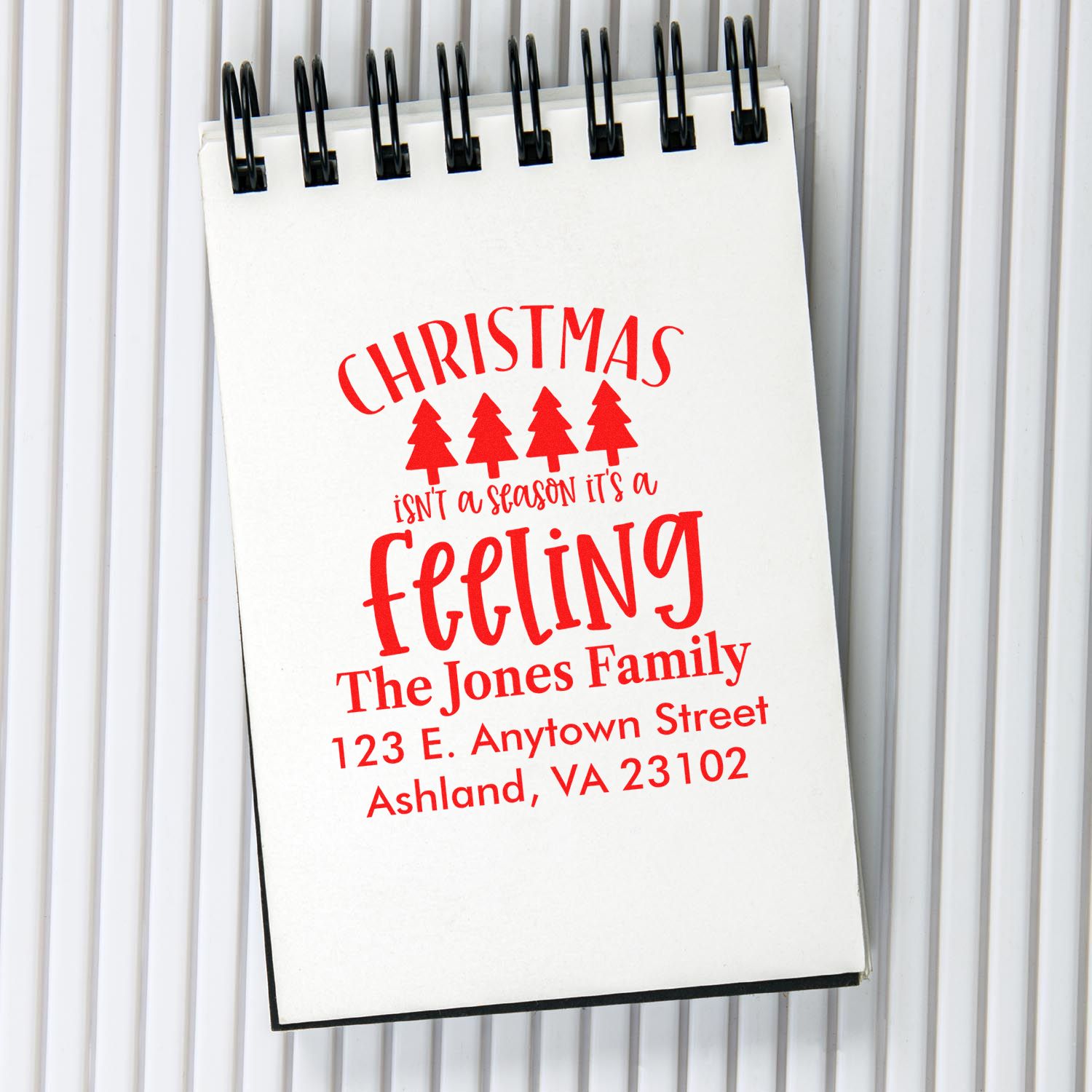 Personalized Christmas return address rubber stamp mockup with festive red text for The Jones Family on a spiral notebook.