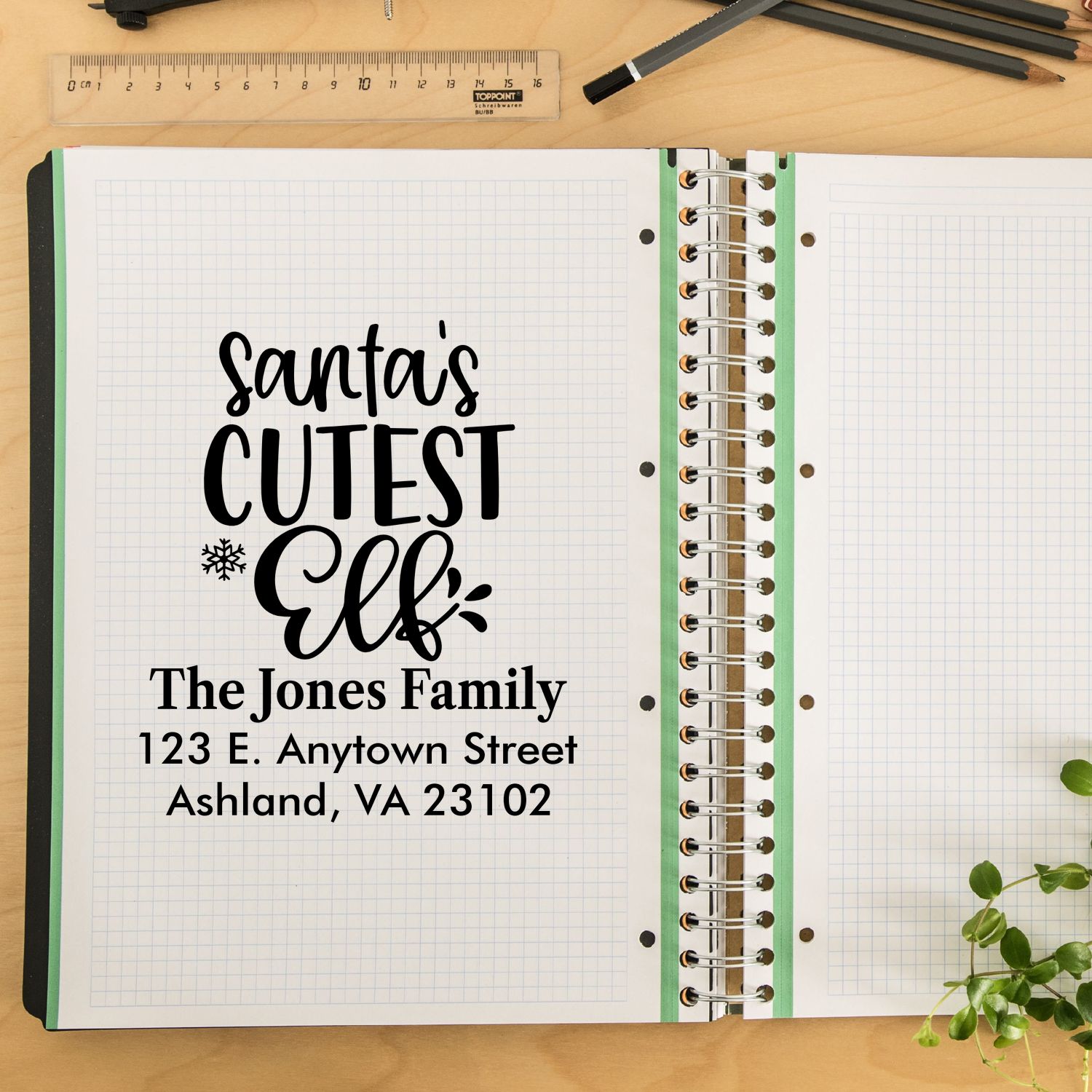 Personalized Christmas rubber stamp mockup with Santas Cutest Elf family address design on notebook page.