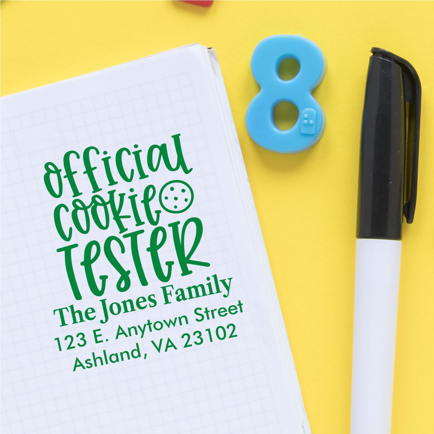 Personalized rubber stamp mockup reading Official Cookie Tester with family name and address on notebook.