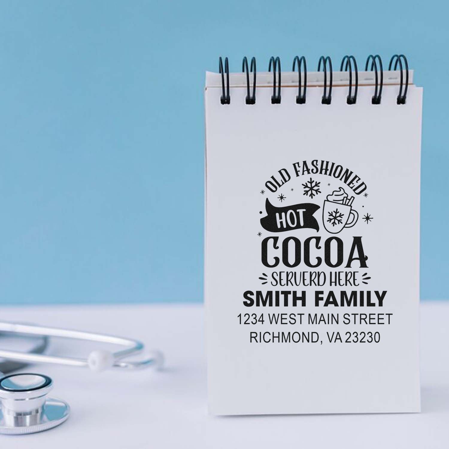 Custom rubber stamp for hot cocoa signs, featuring family name and address on a spiral notebook page.