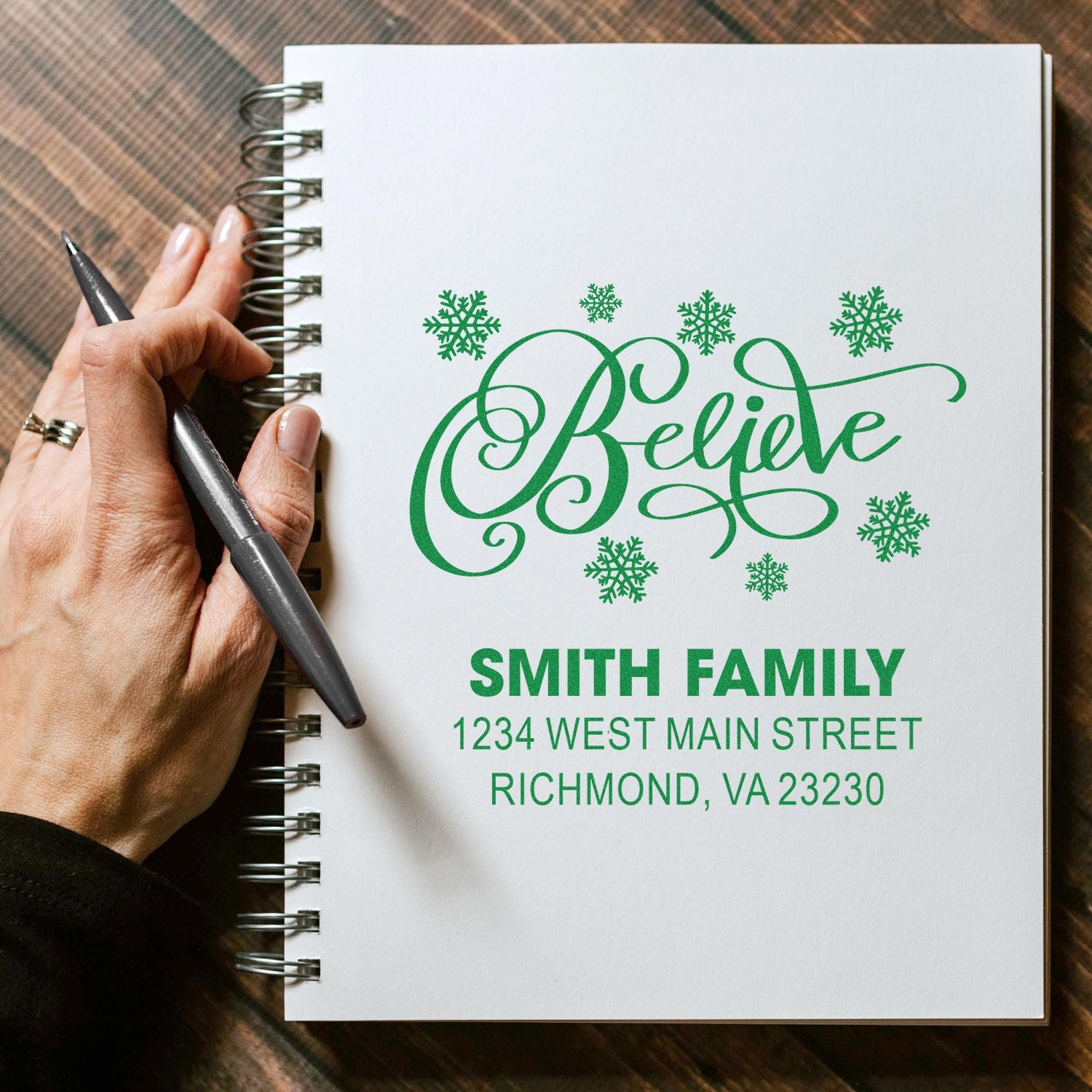 Custom Christmas rubber stamp with Believe script, snowflakes, and Smith Family return address on a notebook page.