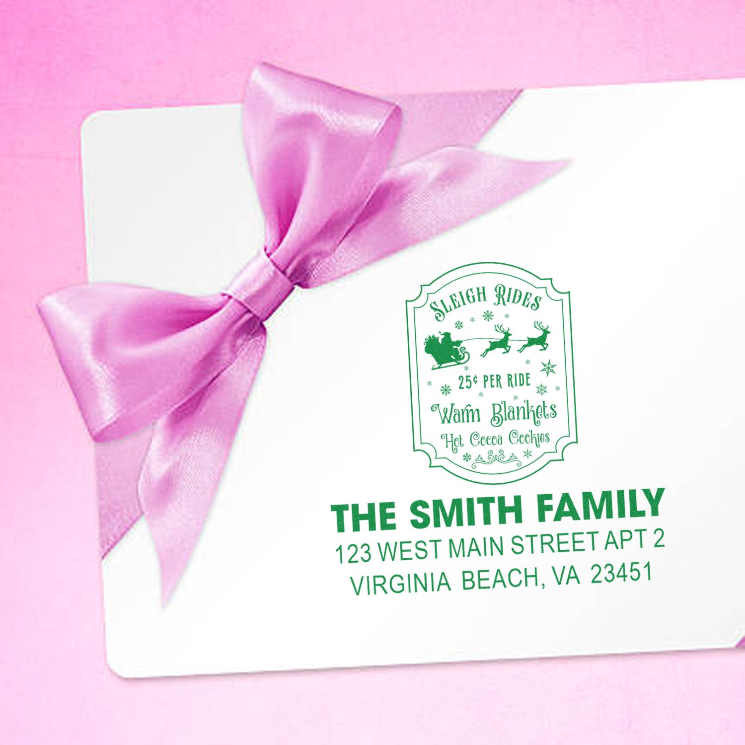 Personalized Christmas rubber stamp on holiday envelope with return address and sleigh rides design, tied with pink ribbon.