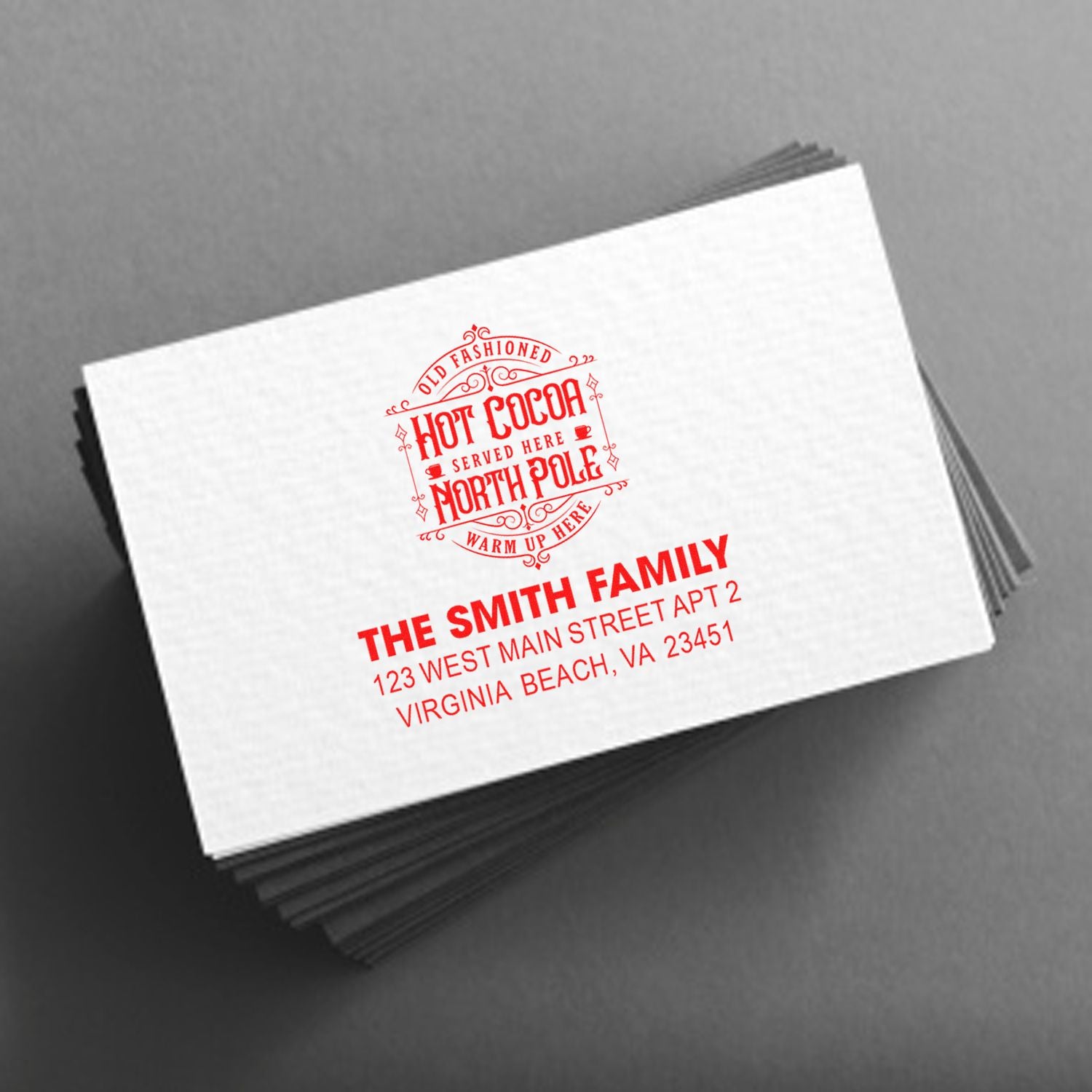 Custom return address rubber stamp design with Hot Cocoa North Pole motif on stacked white envelopes.