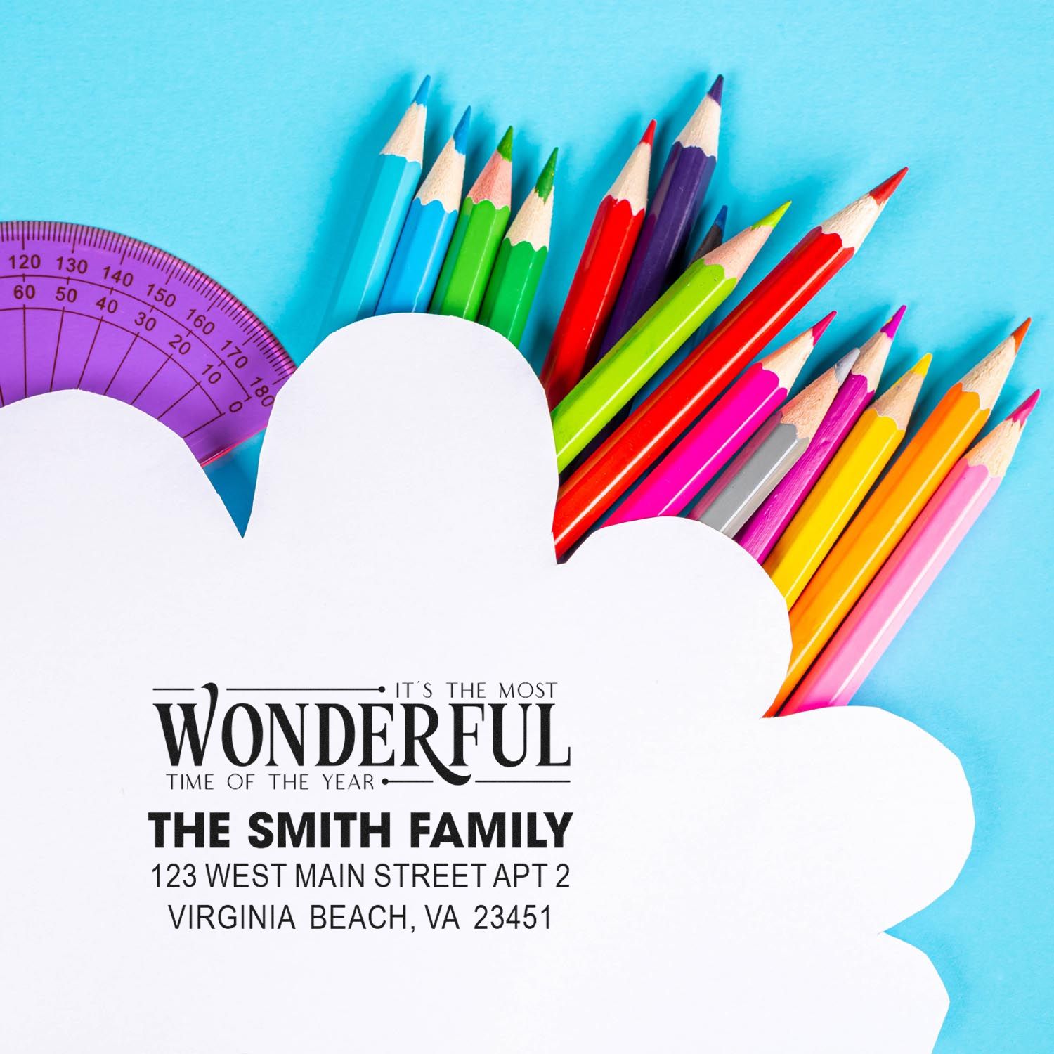 Custom family return address rubber stamp with holiday greeting, surrounded by colorful pencils and a protractor.
